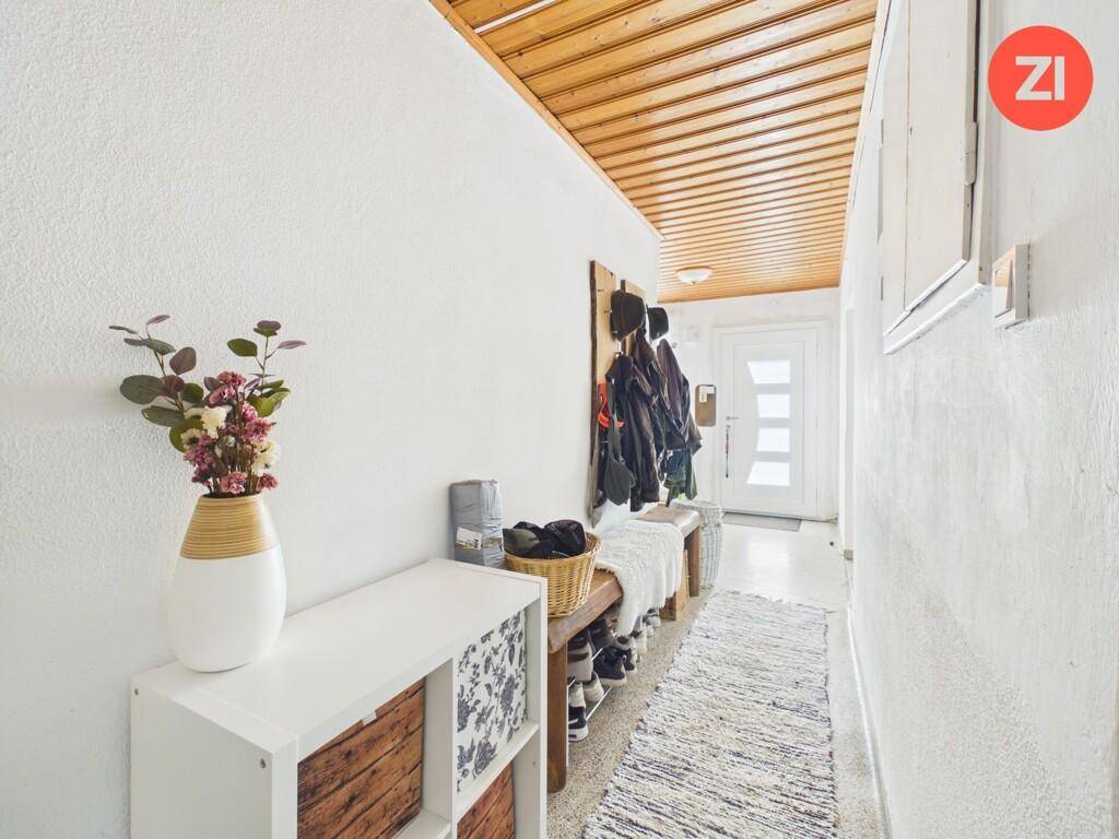 Schmaler Flur mit Holzdecke, Garderobe und Schuhregal am Eingangsbereich.