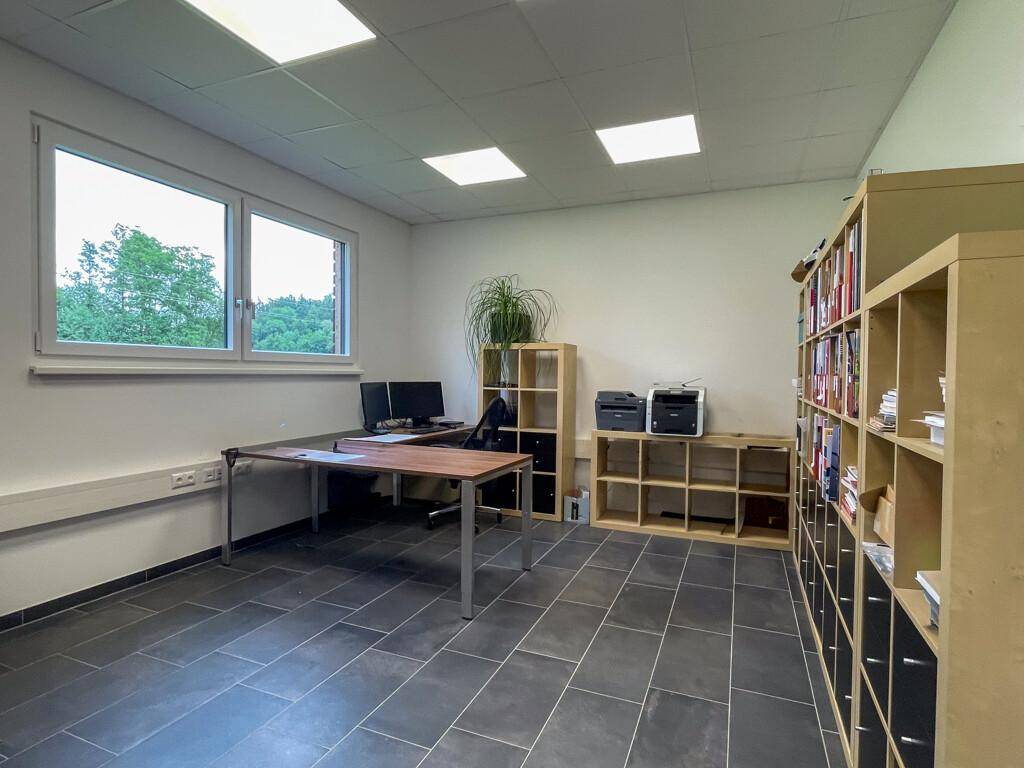 Büroraum mit dunklem Fliesenboden, Holzregalen und Fenstern, die Tageslicht hereinlassen.