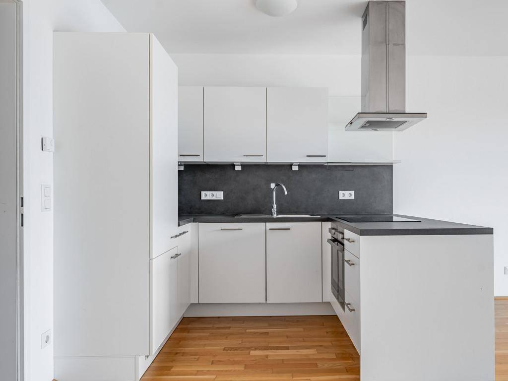 Moderne, weiße Einbauküche mit dunkler Arbeitsplatte und Holzboden in neuwertigem Zustand.