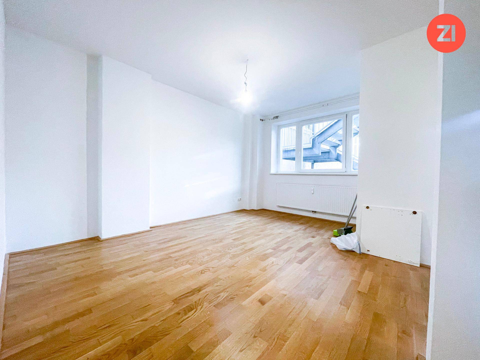 Heller Wohnraum mit Parkettboden und großem Fenster, bietet viel Platz für individuelle Gestaltung.
