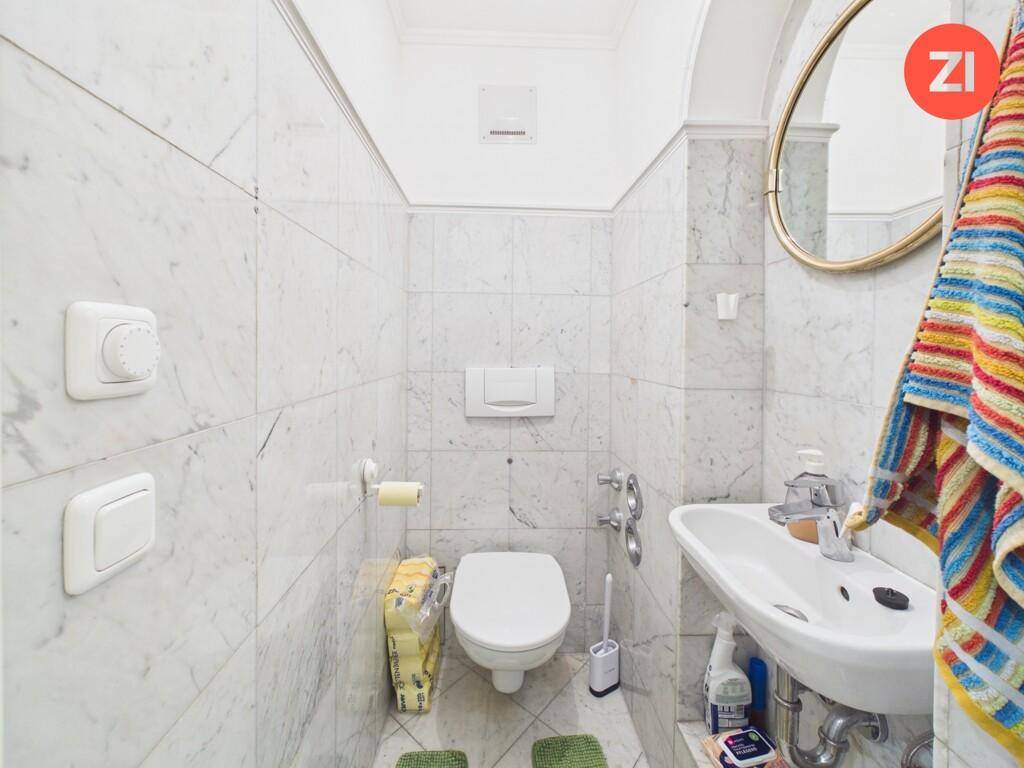 Separates WC mit Toilette, Waschbecken und eleganten Marmorfliesen an den Wänden.