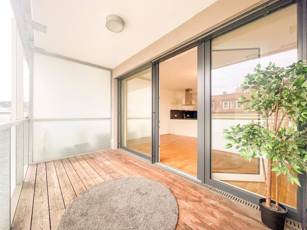 Balkon mit Holzdielenboden, großen Glasschiebetüren und Blick auf die Umgebung.