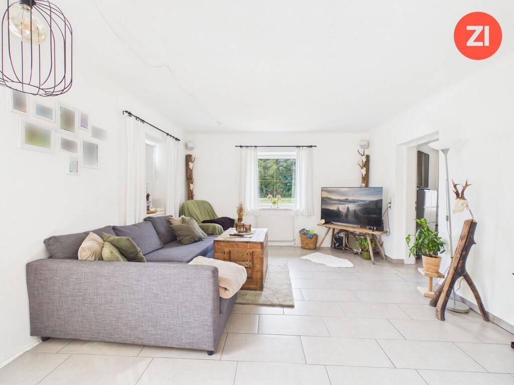 Helles Wohnzimmer mit großem Sofa, Fernseher und Blick in den Garten.