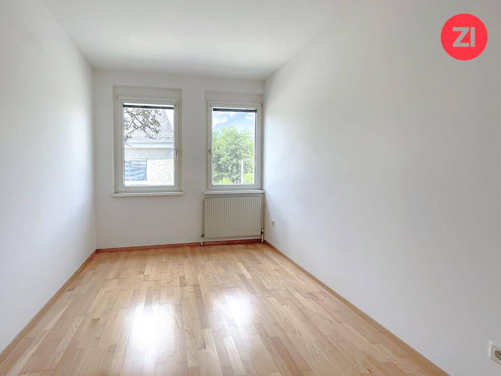 Helles Schlafzimmer mit Holzfußboden, weißen Wänden und zwei Fenstern für natürliche Belichtung.