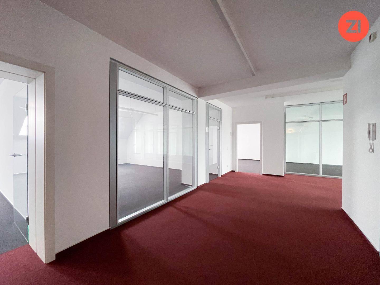 Büroraum mit rotem Teppichboden und Glaswänden, die separate Arbeitsbereiche schaffen.