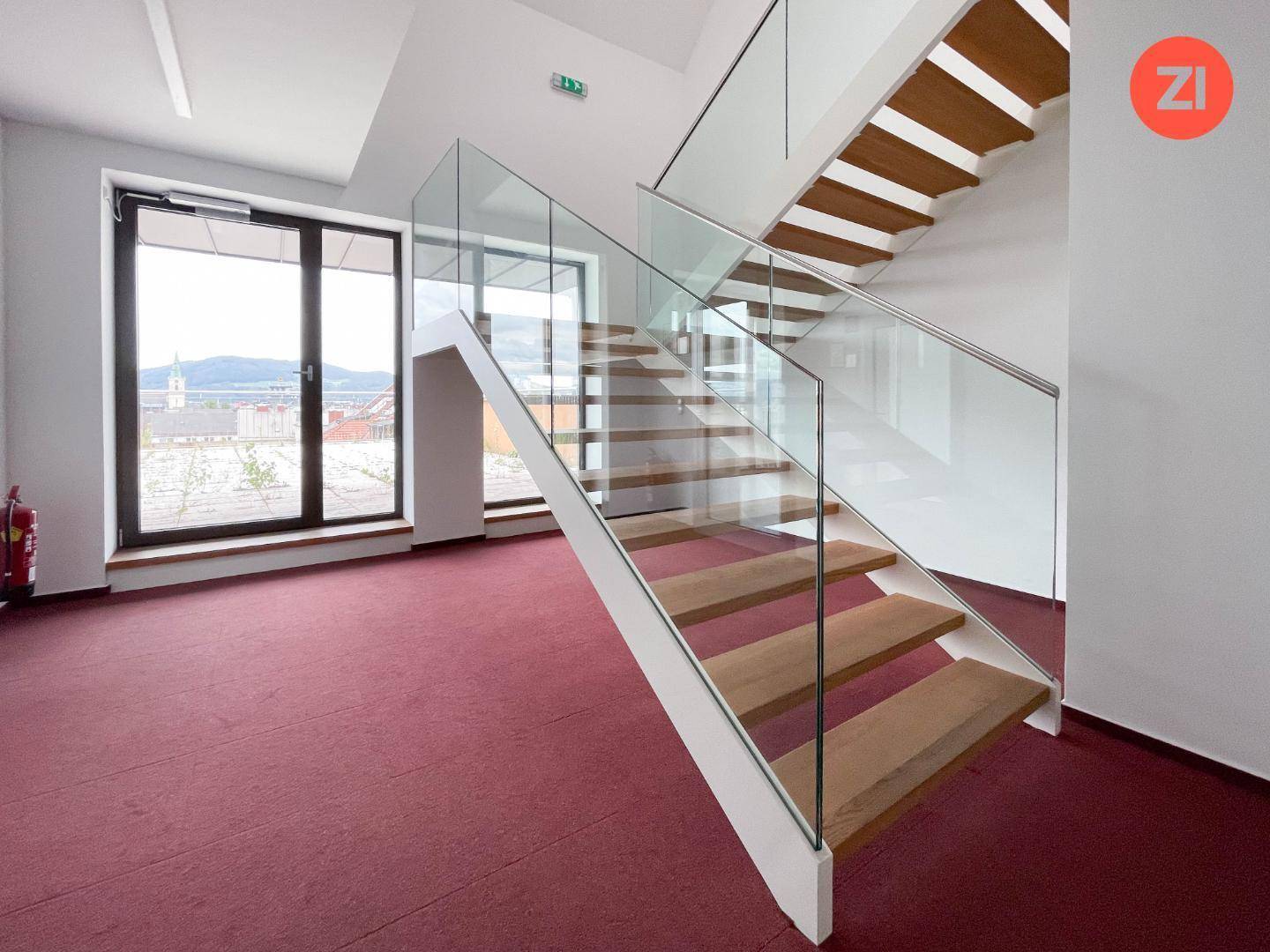 Elegante Holztreppe mit Glasgeländer und rotem Teppichboden in einem modernen Gebäude.