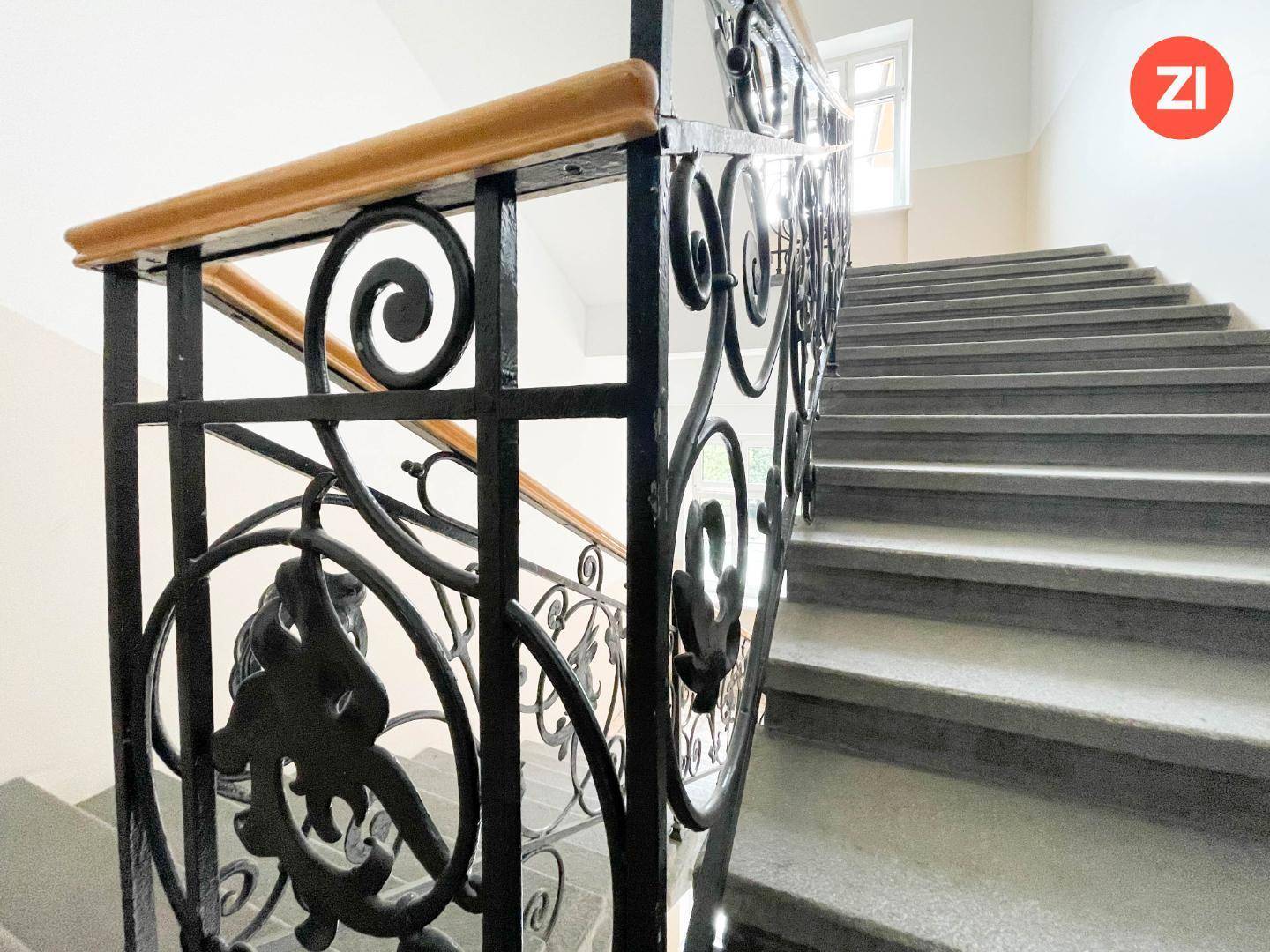 Klassisches Treppenhaus mit Steinstufen und einem kunstvoll geschmiedeten Geländer.