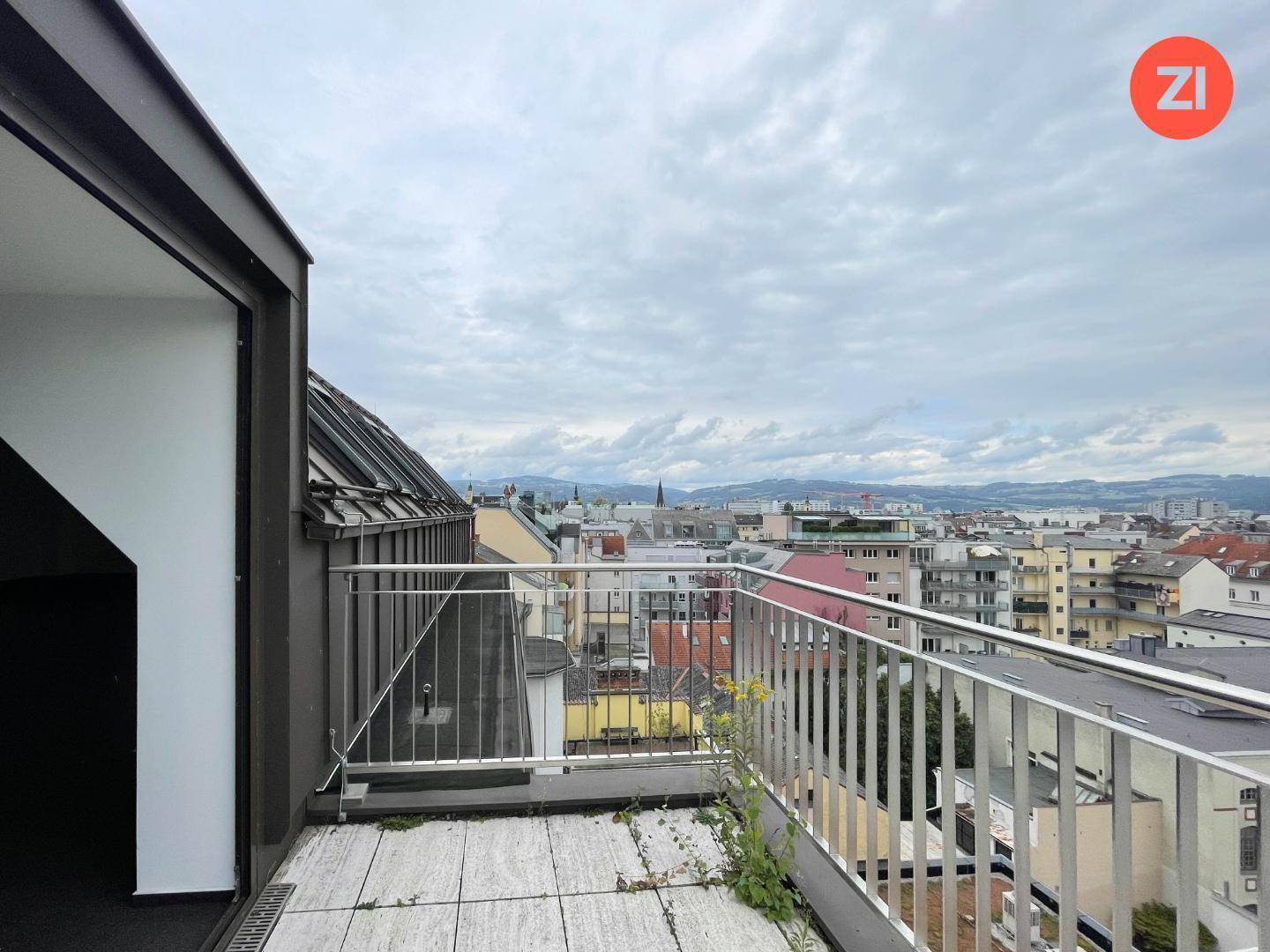 Kleiner Balkon mit Metallgeländer und Panoramablick auf die Stadt und die Dächer.