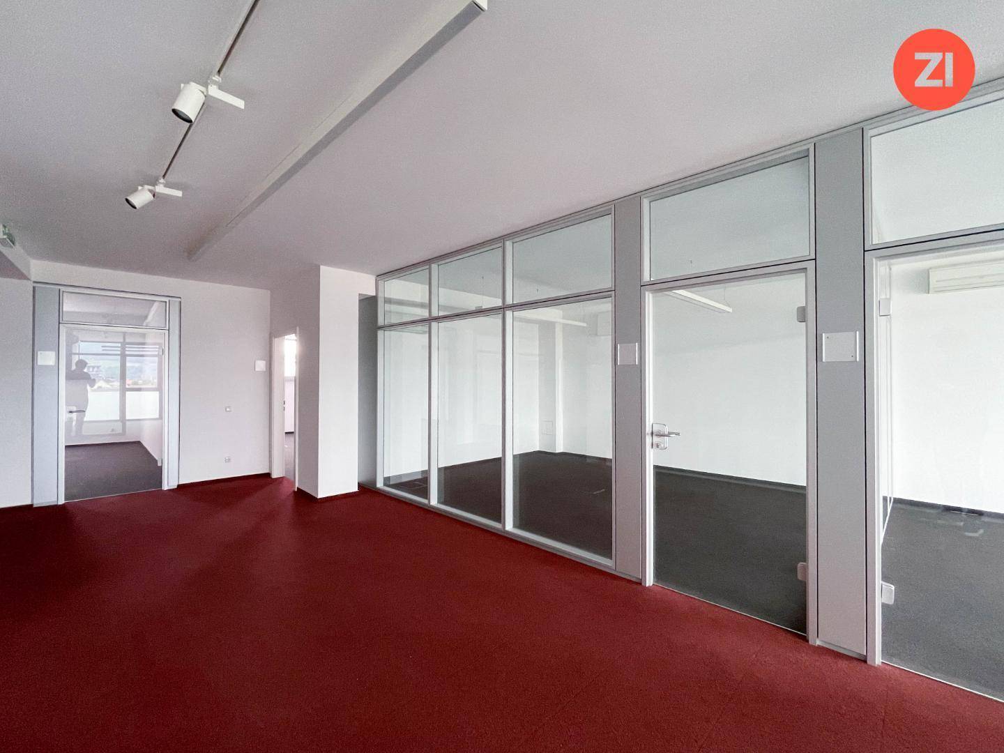 Büroraum mit rotem Teppichboden und Glaswänden, die flexible Arbeitsbereiche ermöglichen.