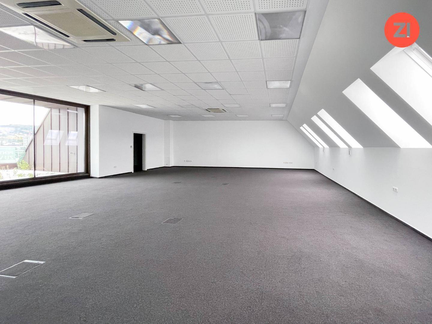Heller Büroraum mit Teppichboden, Dachfenstern und einer modernen Deckenkonstruktion.
