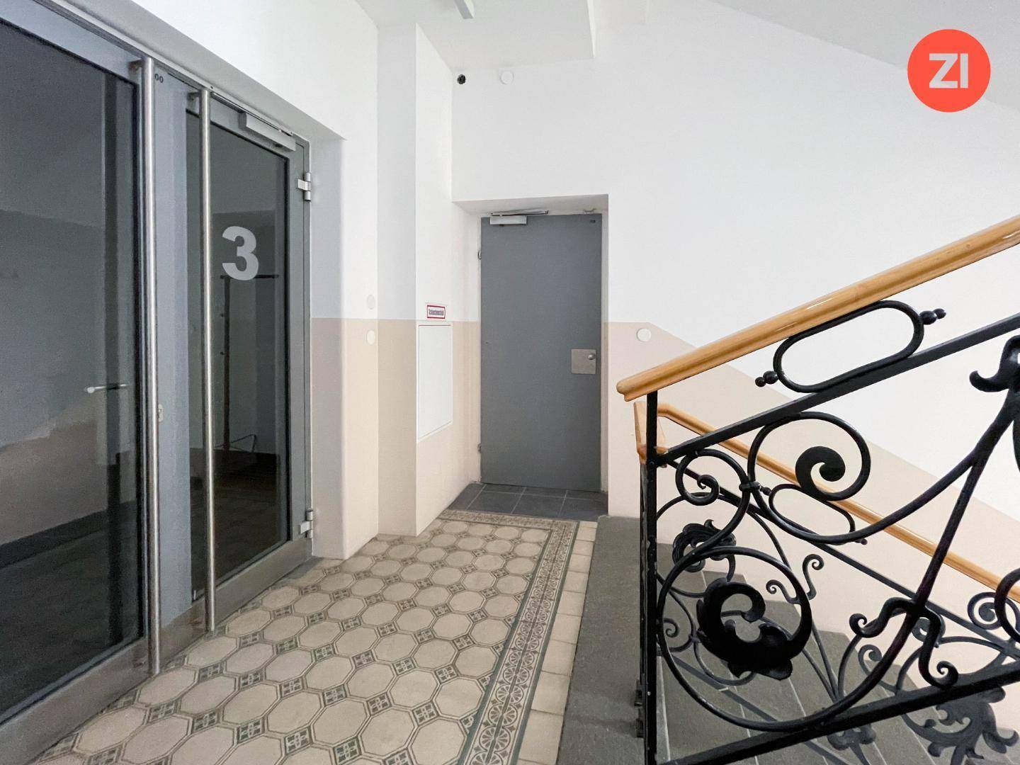 Eingangsbereich mit gemusterten Fliesen, einer verzierten Treppe und Glastüren.