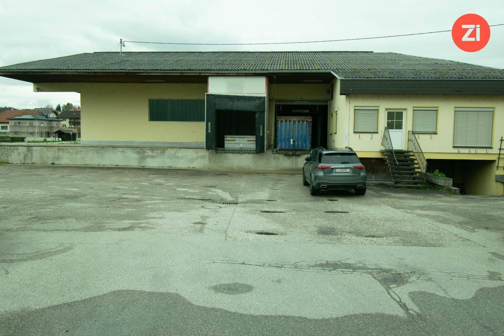 Außenansicht eines Industriegebäudes mit Laderampen, einem geparkten Auto und einer Außentreppe.