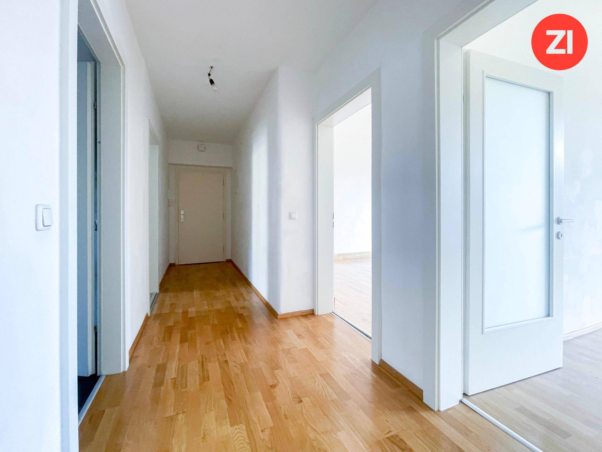 Heller Flur mit Holzboden und weißen Wänden, der zu verschiedenen Zimmern der Wohnung führt.