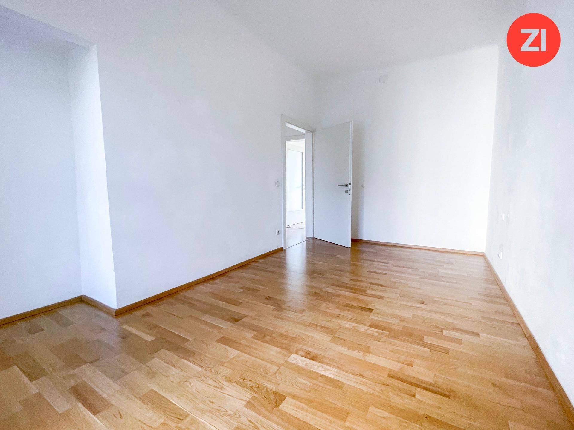 Geräumiger, leerer Wohnraum mit hellem Holzboden und weißen Wänden, bereit zur individuellen Einrichtung.