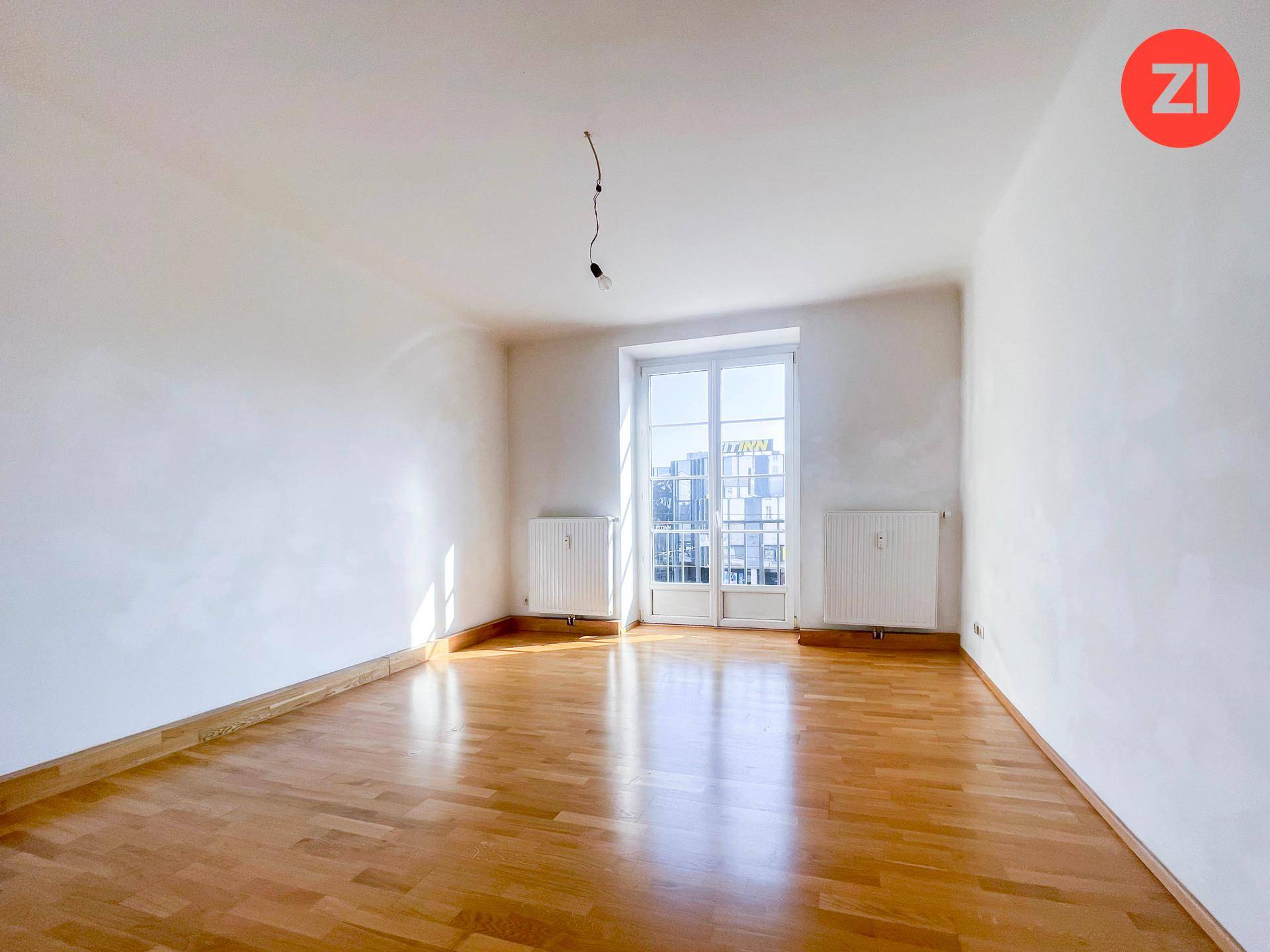 Heller Wohnraum mit Holzboden, weißen Wänden und einem großen Fenster mit französischem Balkon.