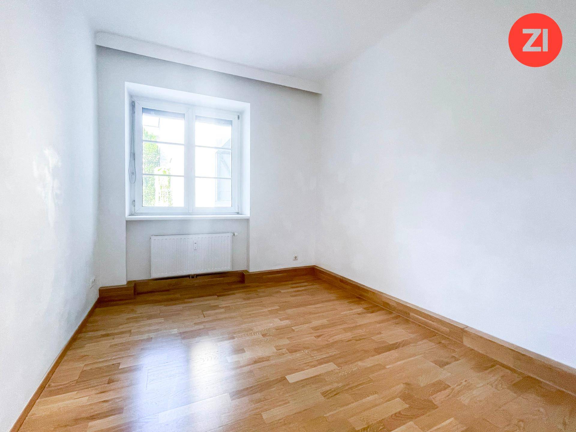 Helles Schlafzimmer mit Holzboden, weißen Wänden und einem Fenster, das viel Tageslicht hereinlässt.