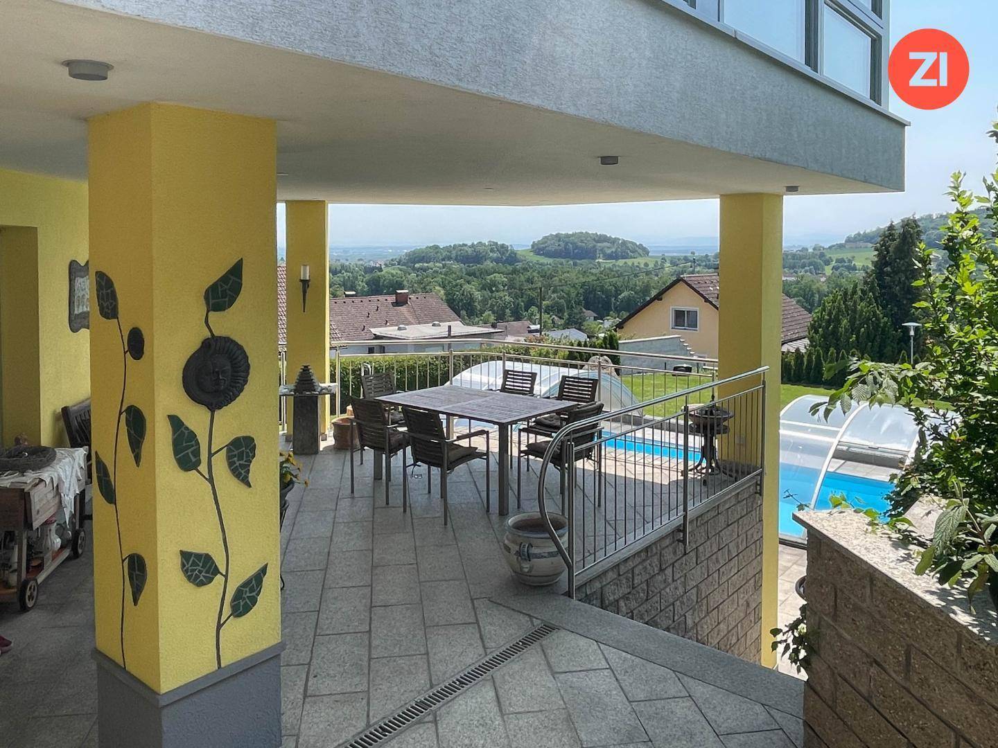 Überdachte Terrasse mit dekorativen Elementen und weitem Blick auf den Pool und die Landschaft.