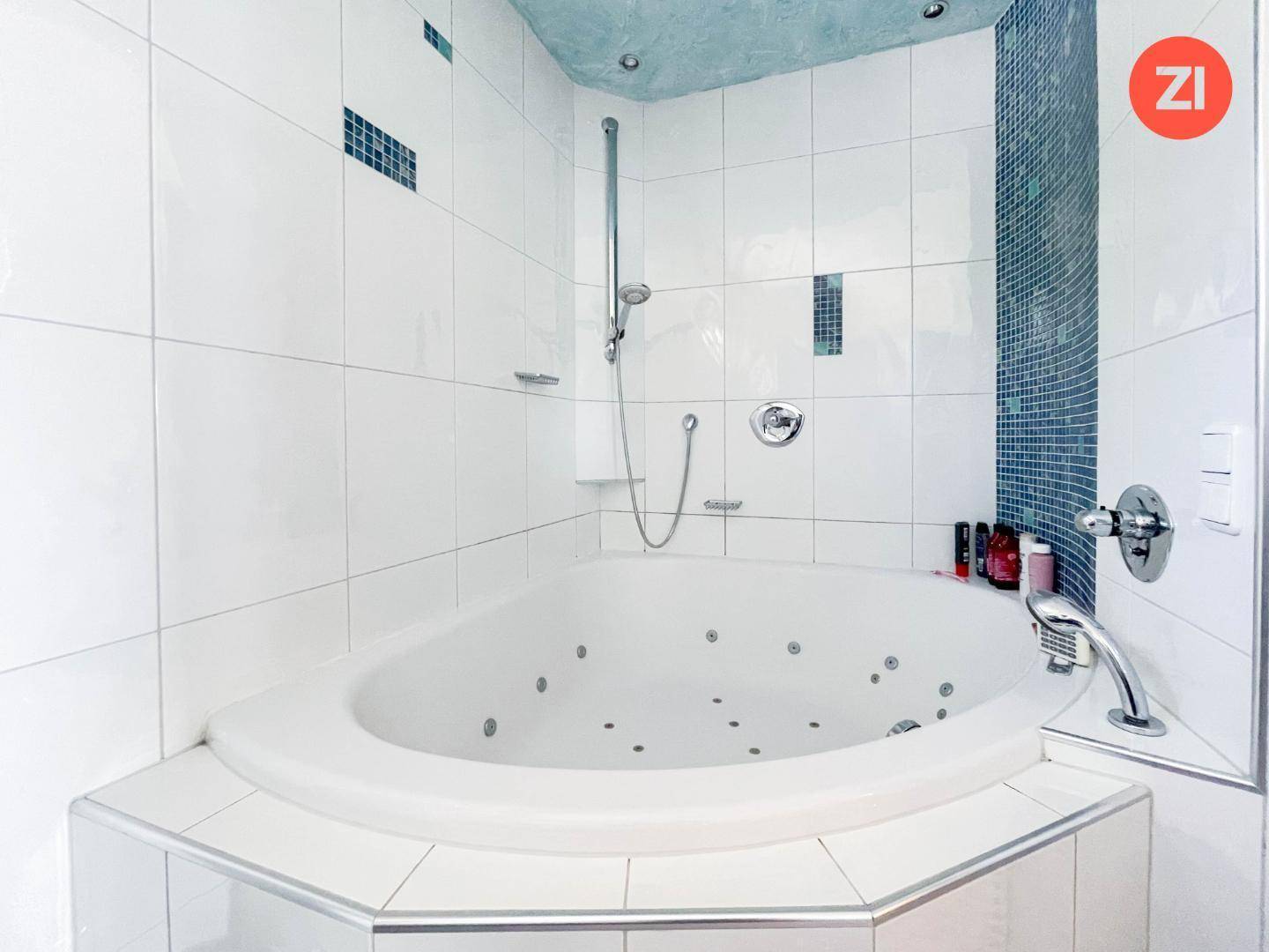 Modernes Badezimmer mit Eck-Whirlpool-Badewanne und Duschfunktion, umgeben von weißen Fliesen.