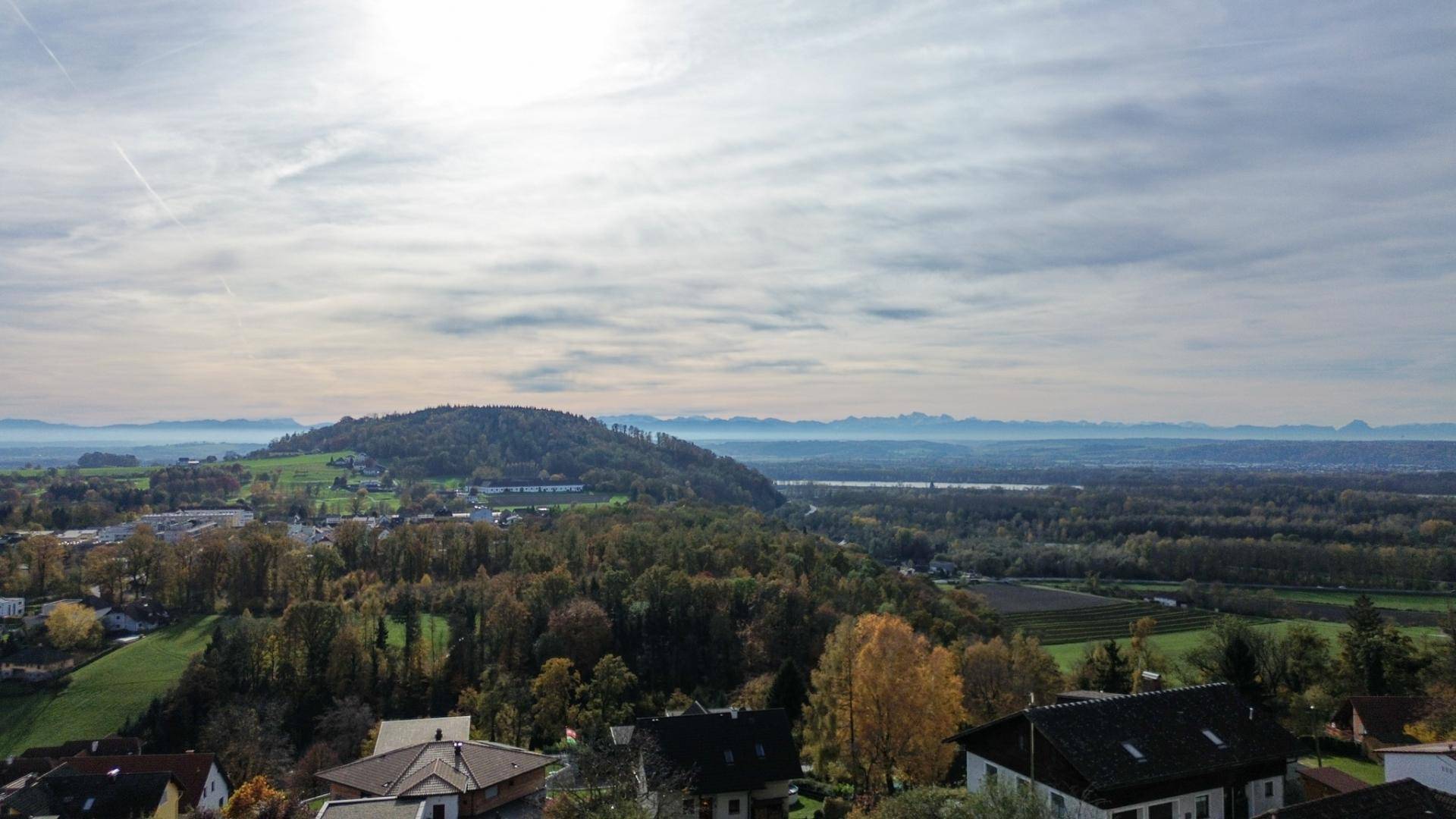 Panoramablick über die weite, grüne Landschaft mit Hügeln und einem See in der Ferne.