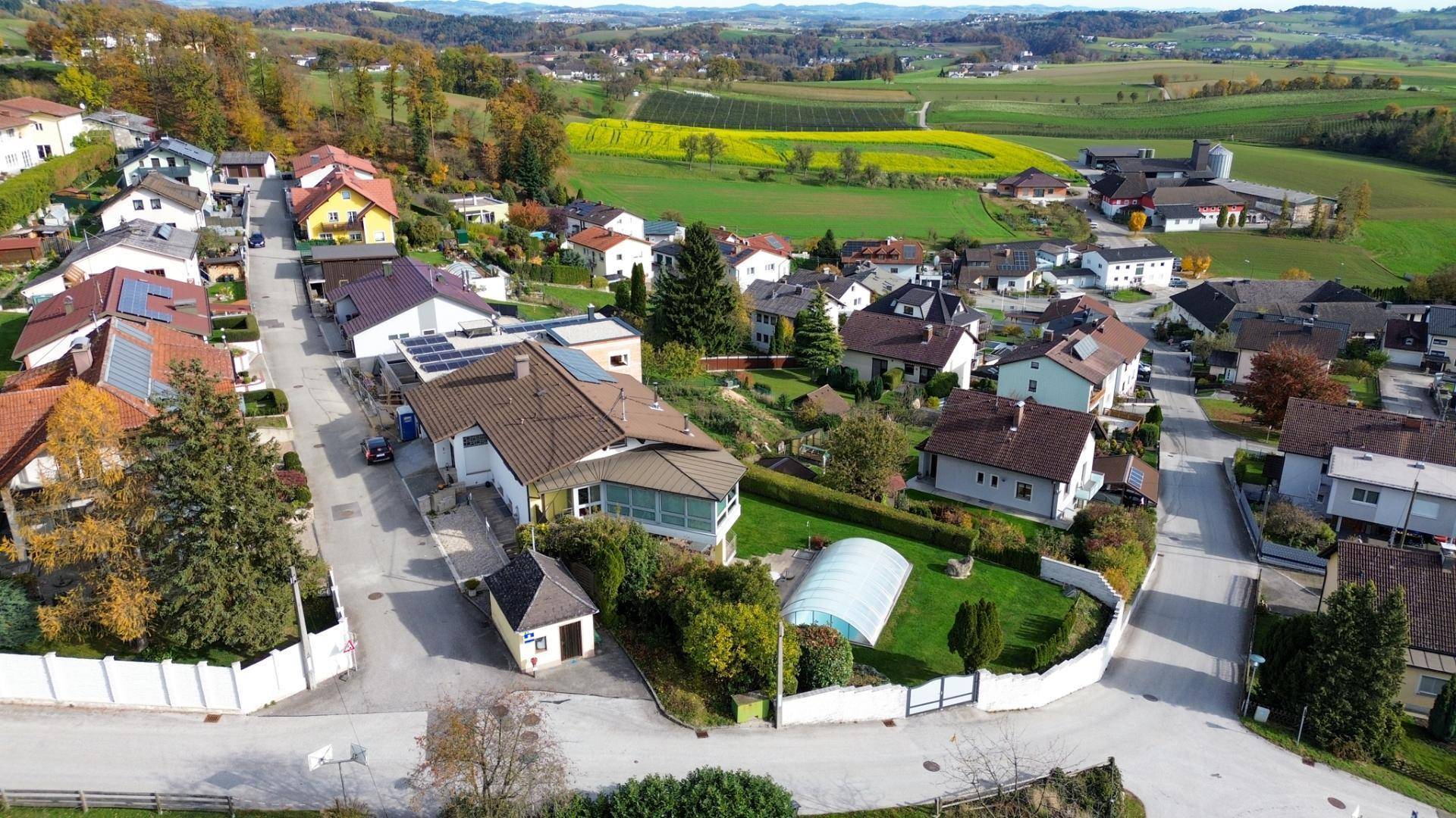 Luftaufnahme einer idyllischen Wohnsiedlung mit Einfamilienhäusern, umgeben von grünen Hügeln und Feldern.