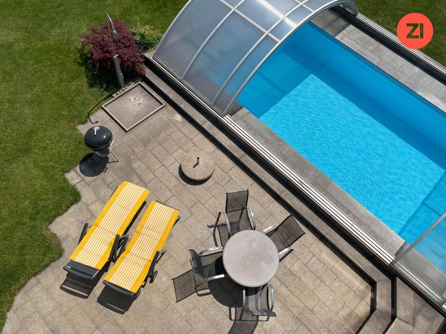 Detailansicht des Poolbereichs mit Liegestühlen, Esstisch und Grill auf der Terrasse.