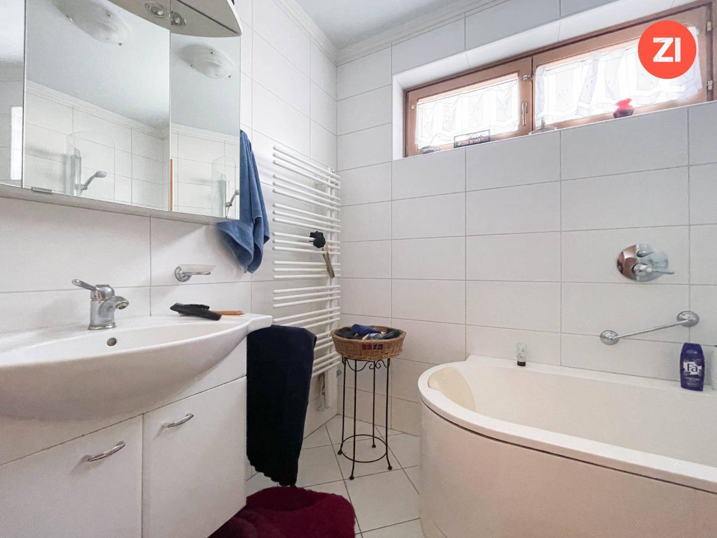 Helles Badezimmer mit Badewanne, Waschbecken, beheiztem Handtuchhalter und Fenster.