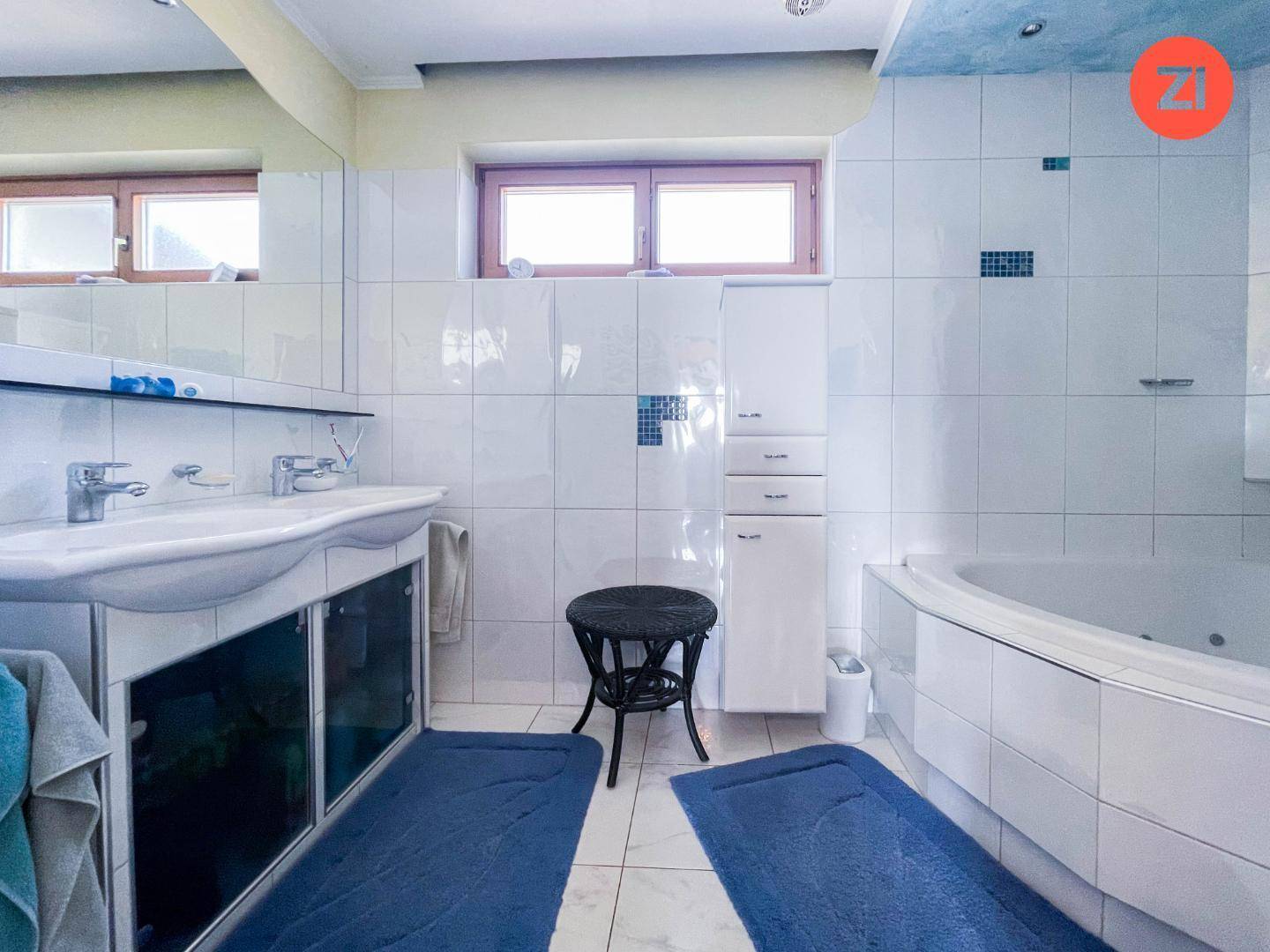 Helles Badezimmer mit Doppelwaschbecken, Whirlpool-Badewanne und weißen Fliesen.