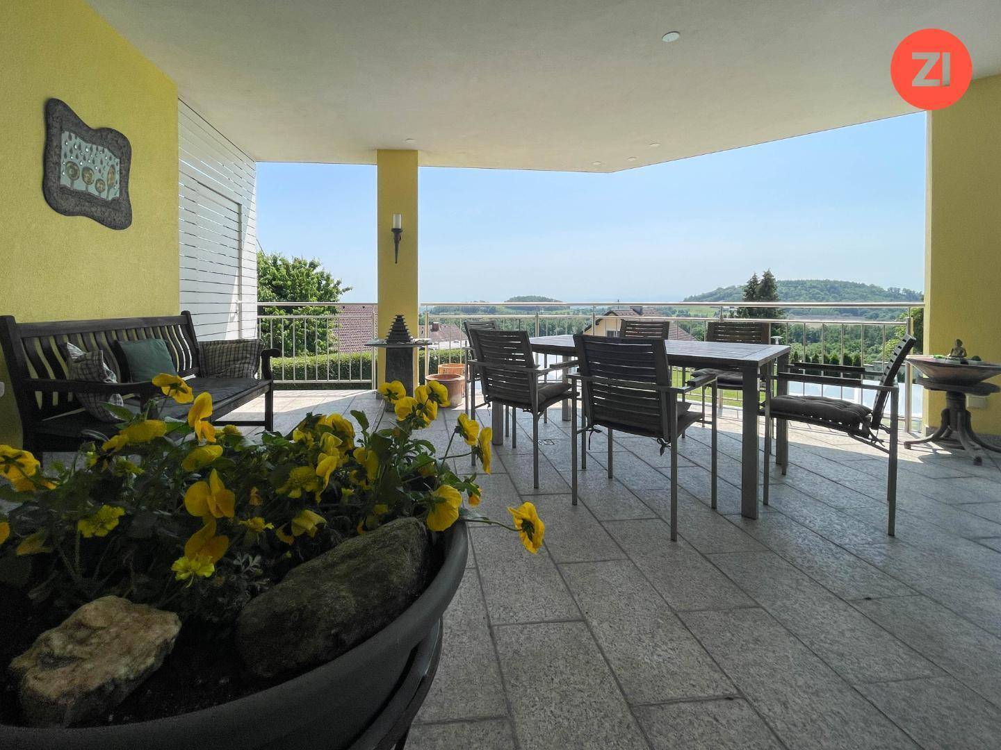 Große überdachte Terrasse mit Essbereich und weitem Blick über die grüne Landschaft.