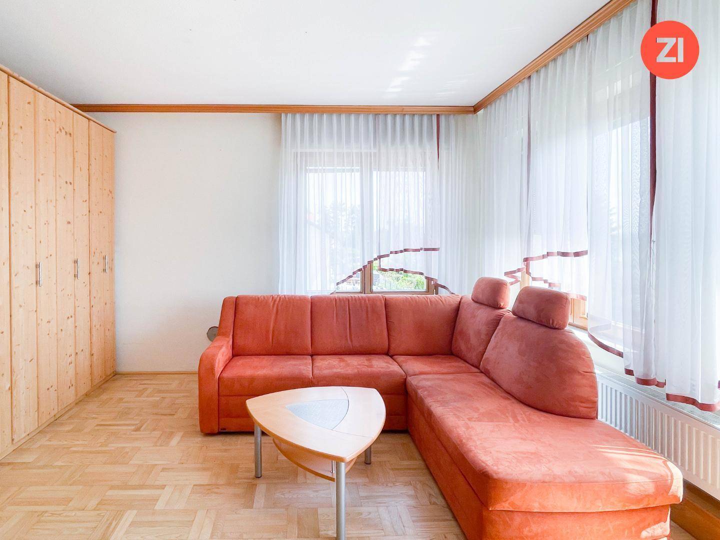 Helles Schlafzimmer mit Holzparkett, großem Ecksofa und viel Tageslicht durch die Fenster.