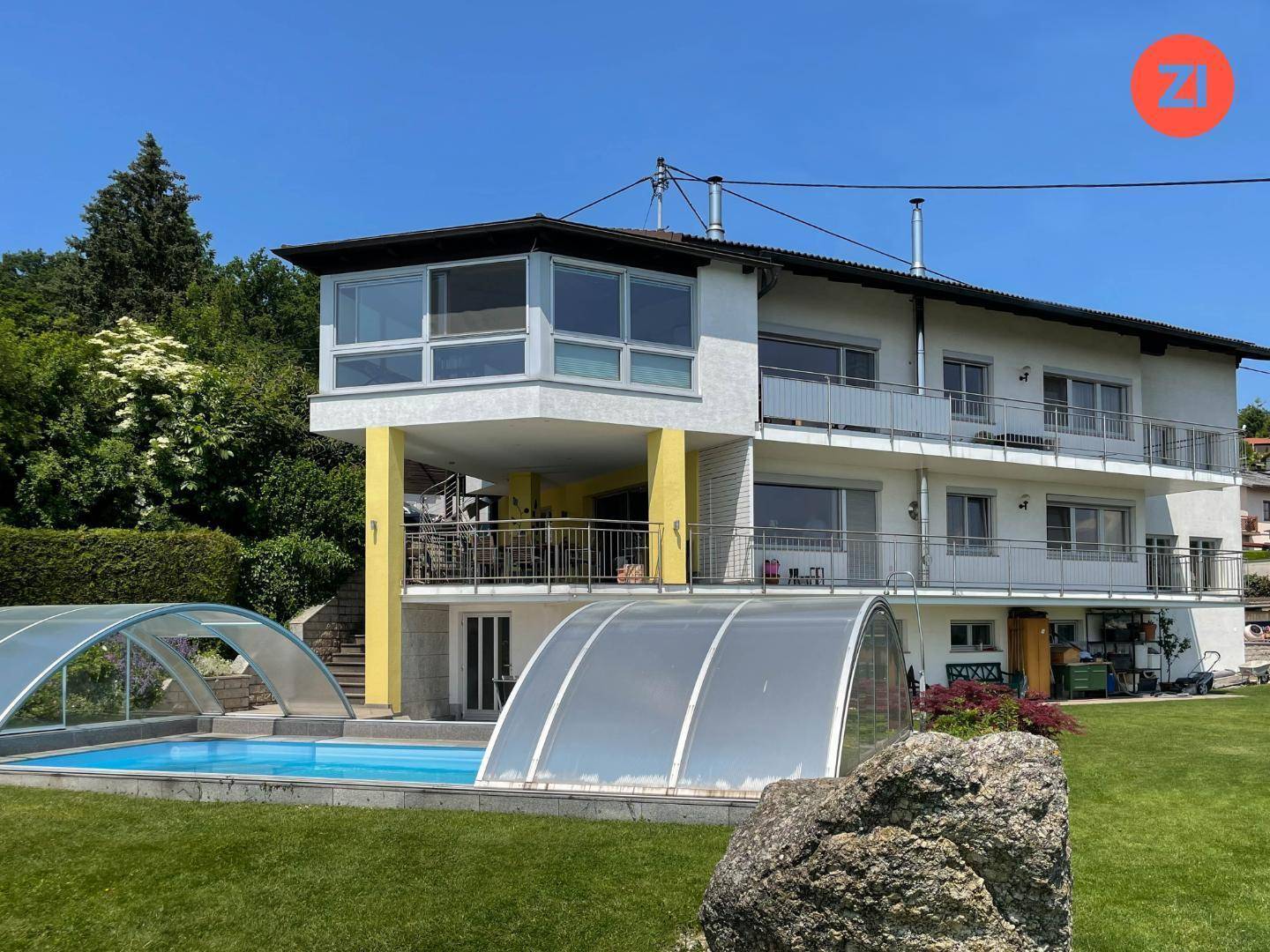 Ansicht des Hauses von der Gartenseite mit großem Pool und mehreren Balkonen.