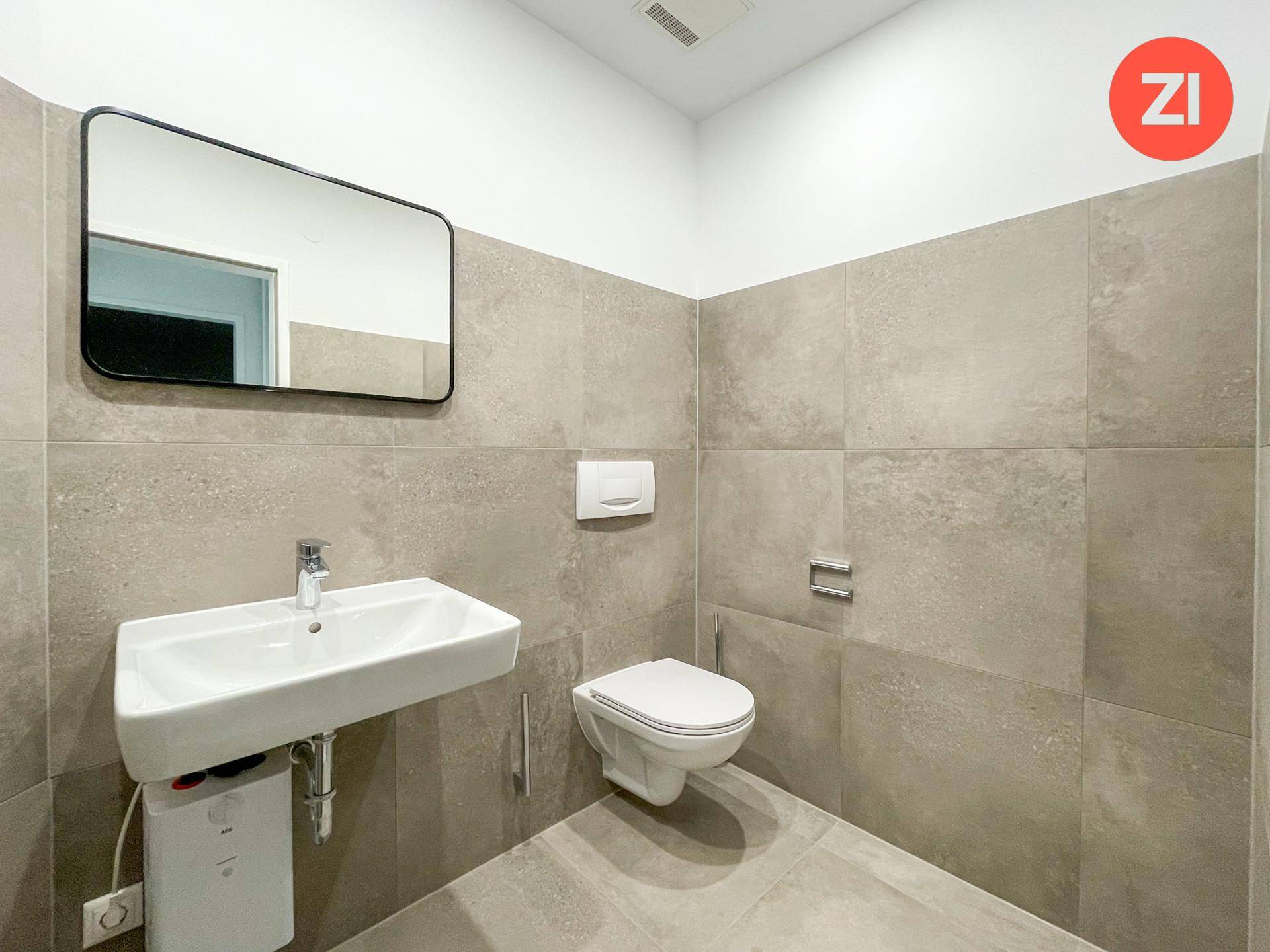 Modernes WC mit grauen Fliesen, wandhängender Toilette und rechteckigem Waschbecken.