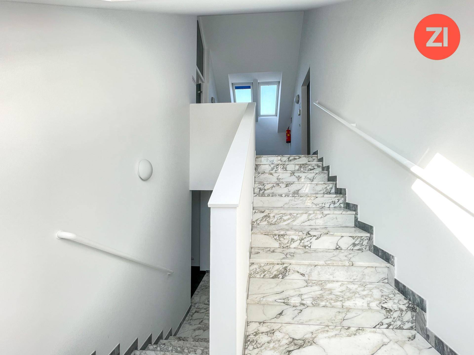 Marmortreppe mit weißem Geländer, die zu den oberen Etagen führt, mit Tageslicht von oben.