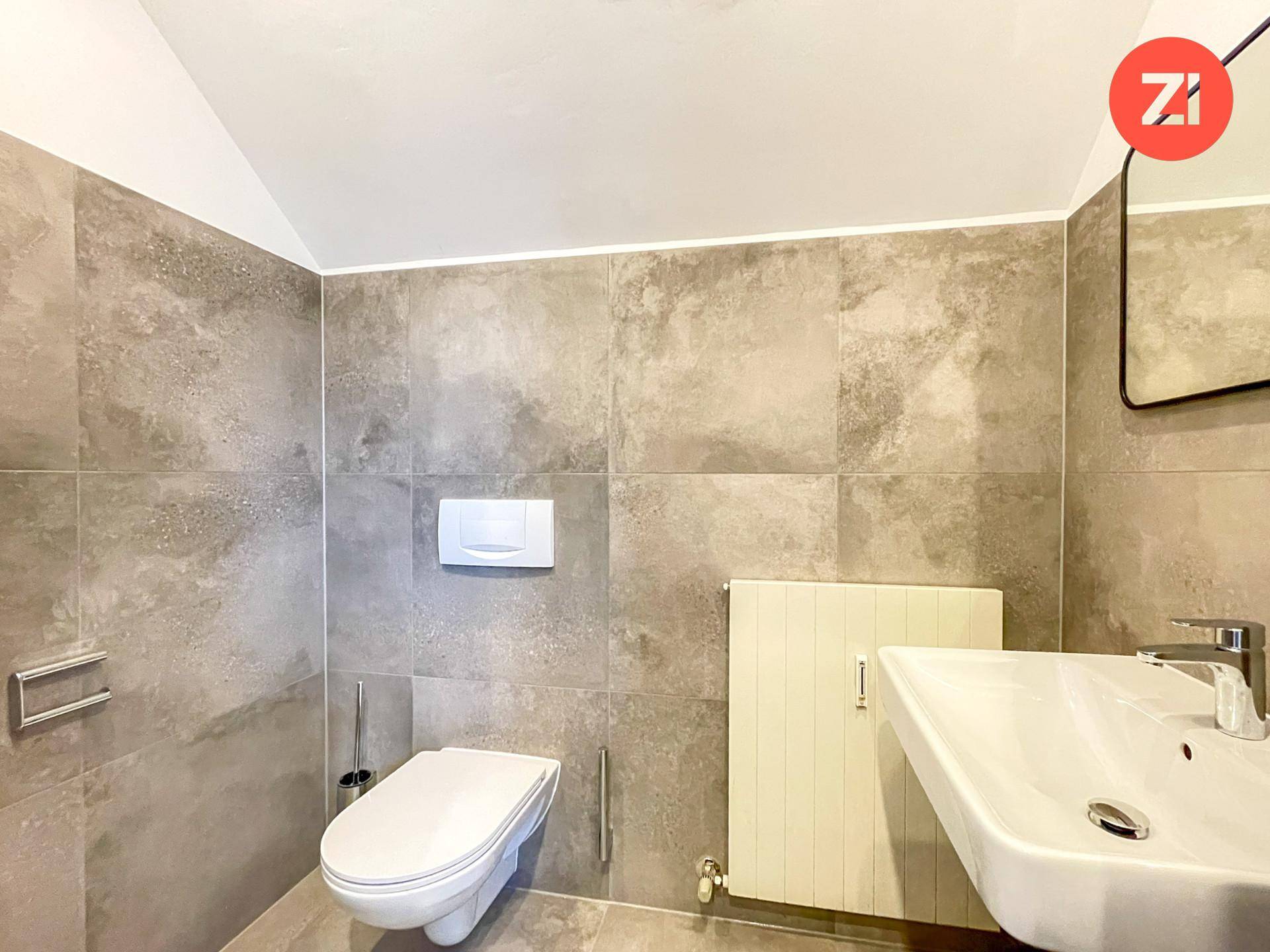 Modernes WC mit grauen Fliesen, wandhängender Toilette und rechteckigem Waschbecken.