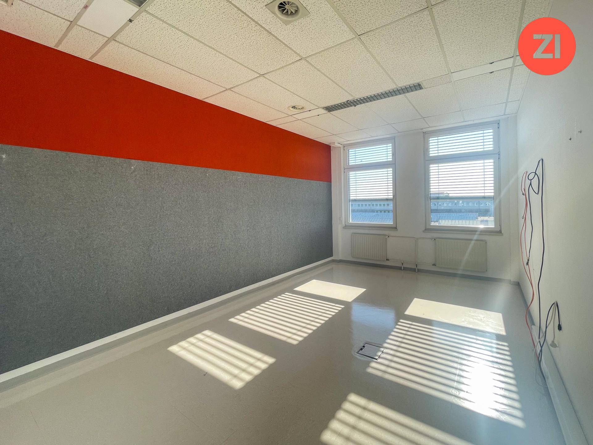 Büroraum mit einer orange-grau gestrichenen Wand, zwei Fenstern und abgehängter Decke.