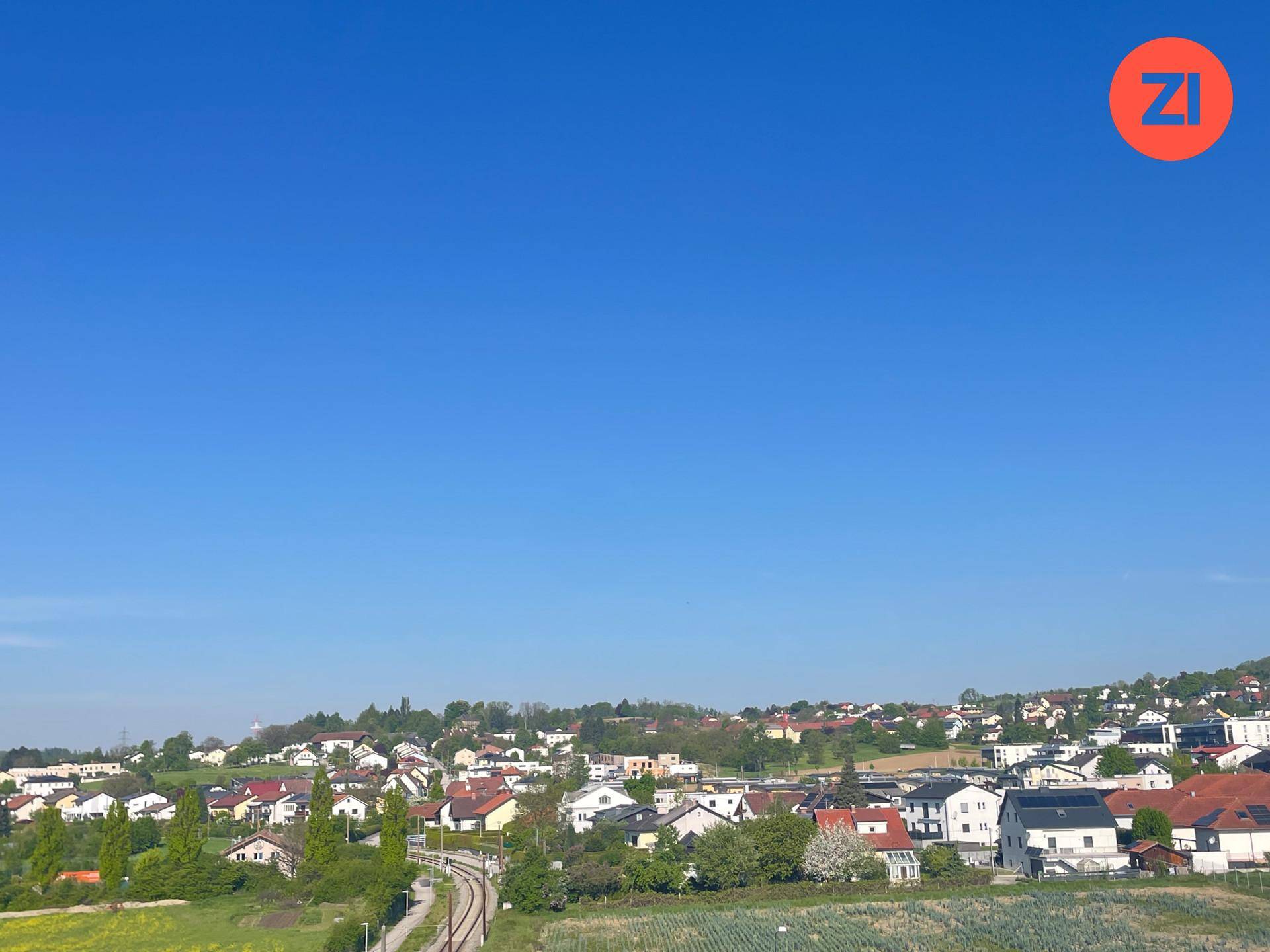 Weitläufige Aussicht auf ein Dorf mit vielen Häusern und grünen Flächen unter klarem blauem Himmel.