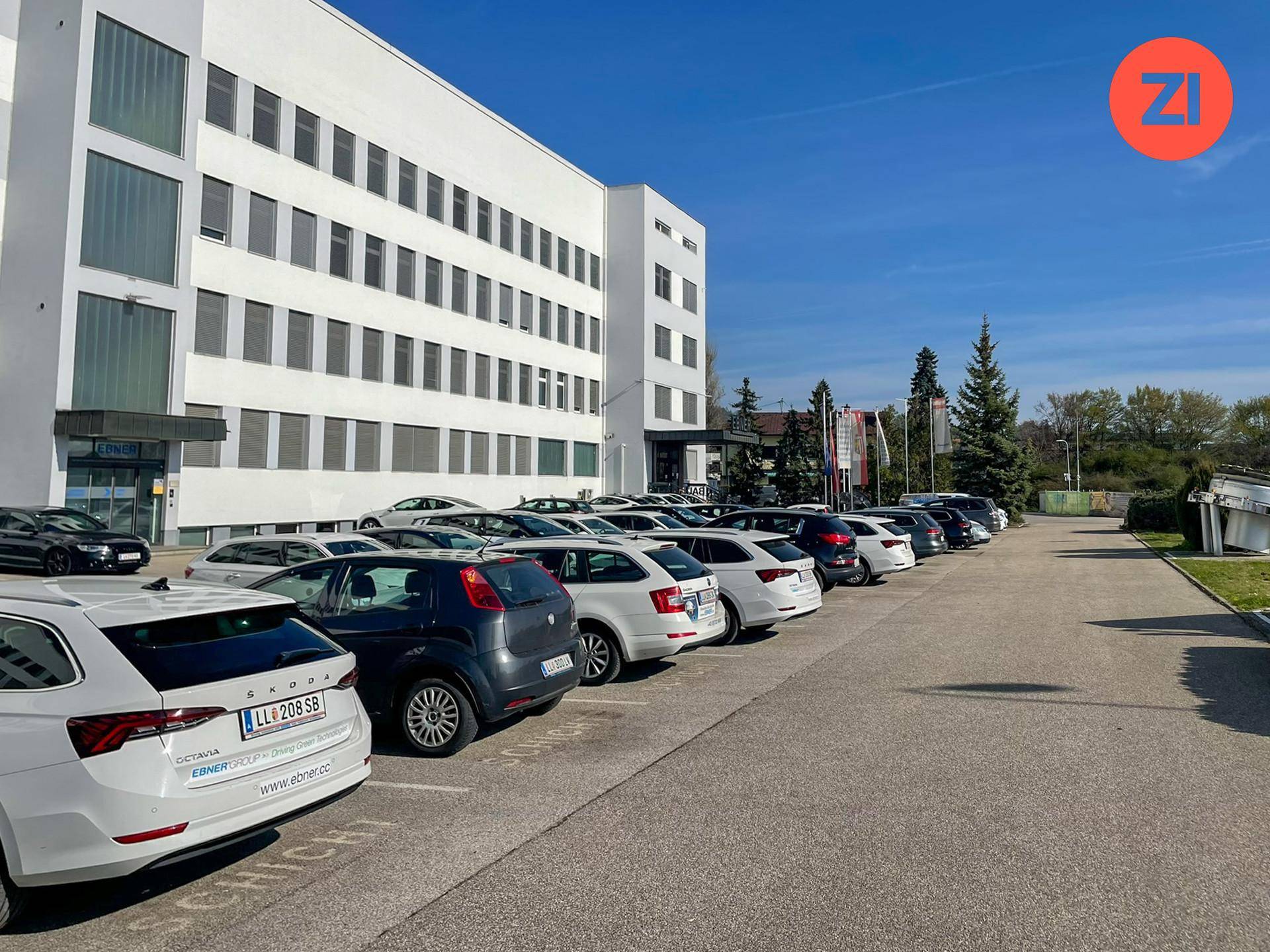 Außenansicht des weißen Gebäudes mit einem großen, gut gefüllten Parkplatz für Mitarbeiter und Besucher.