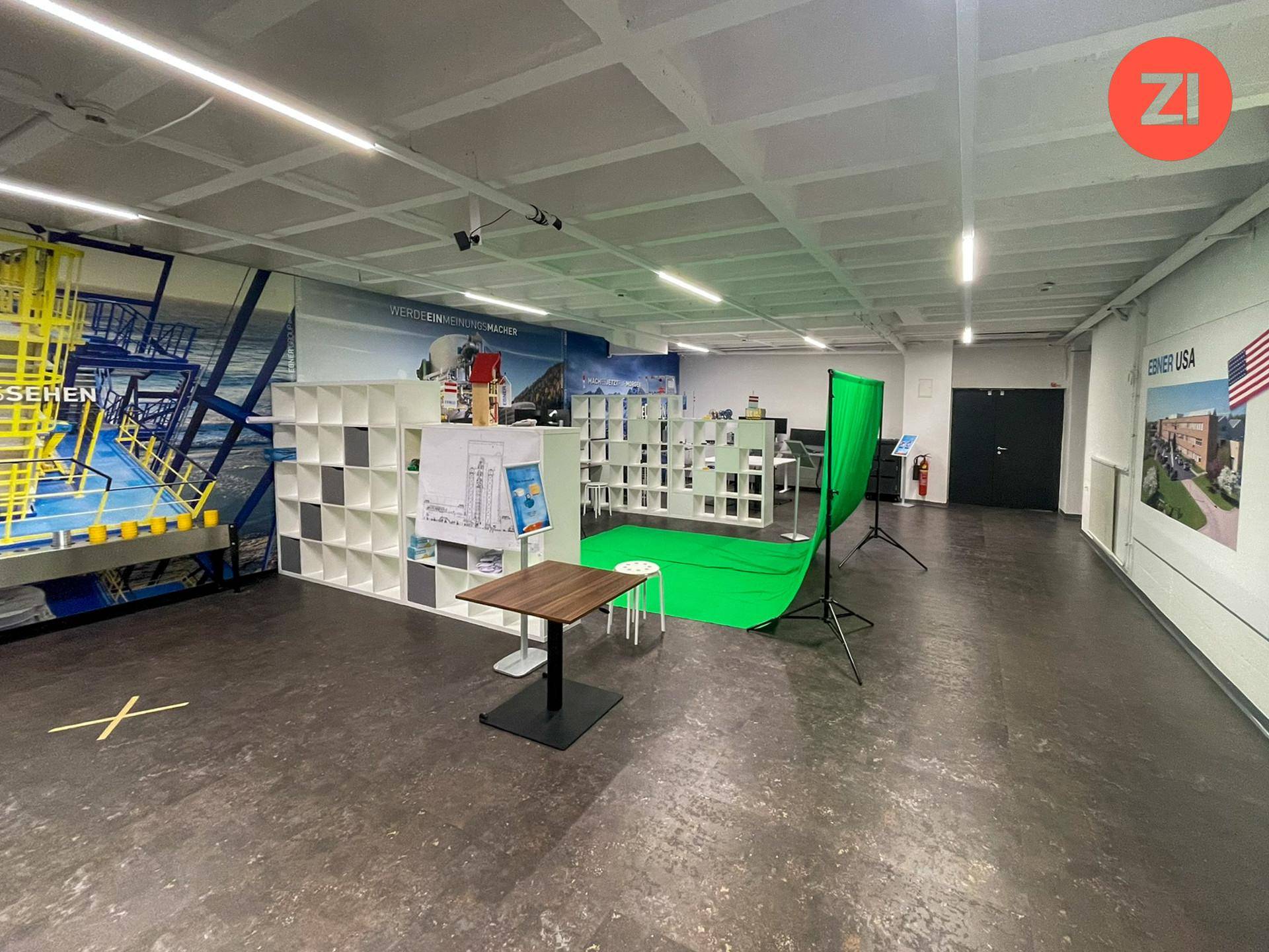 Großer, offener Raum für Präsentationen oder Veranstaltungen mit Greenscreen und Regalen.