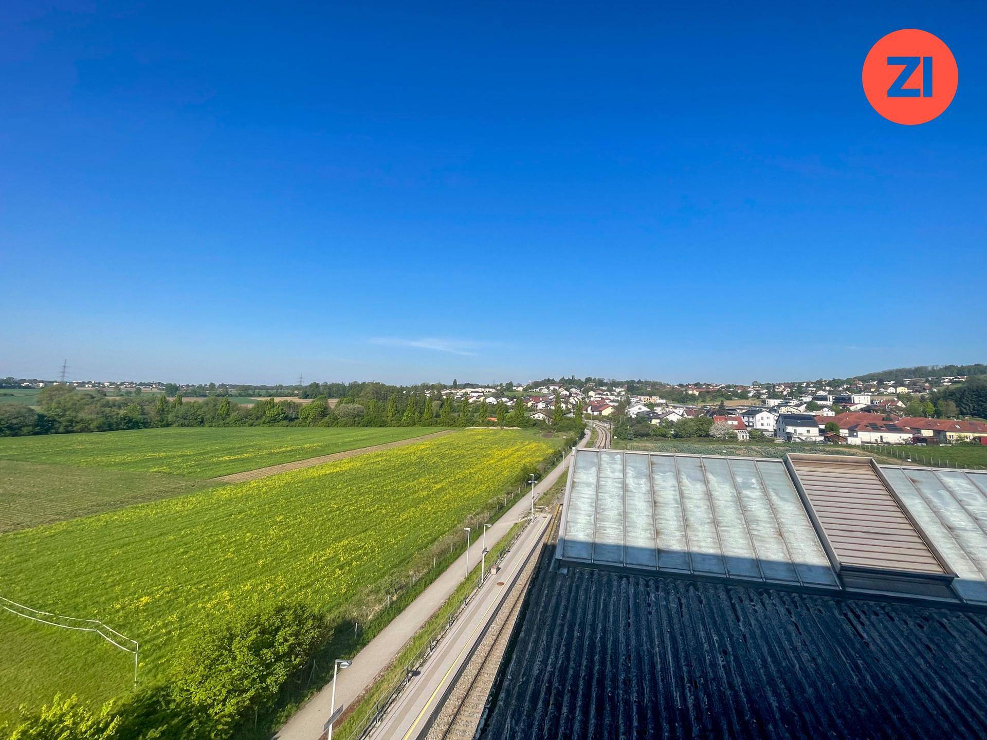 Weitläufige Aussicht auf grüne Felder, Bahngleise und ein Dorf in der Ferne.
