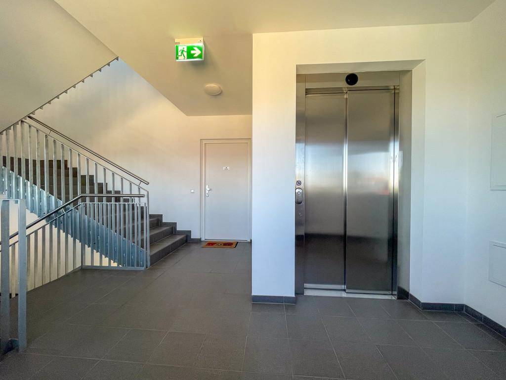 Heller Flur mit modernem Treppenhaus und einem glänzenden Edelstahlaufzug.