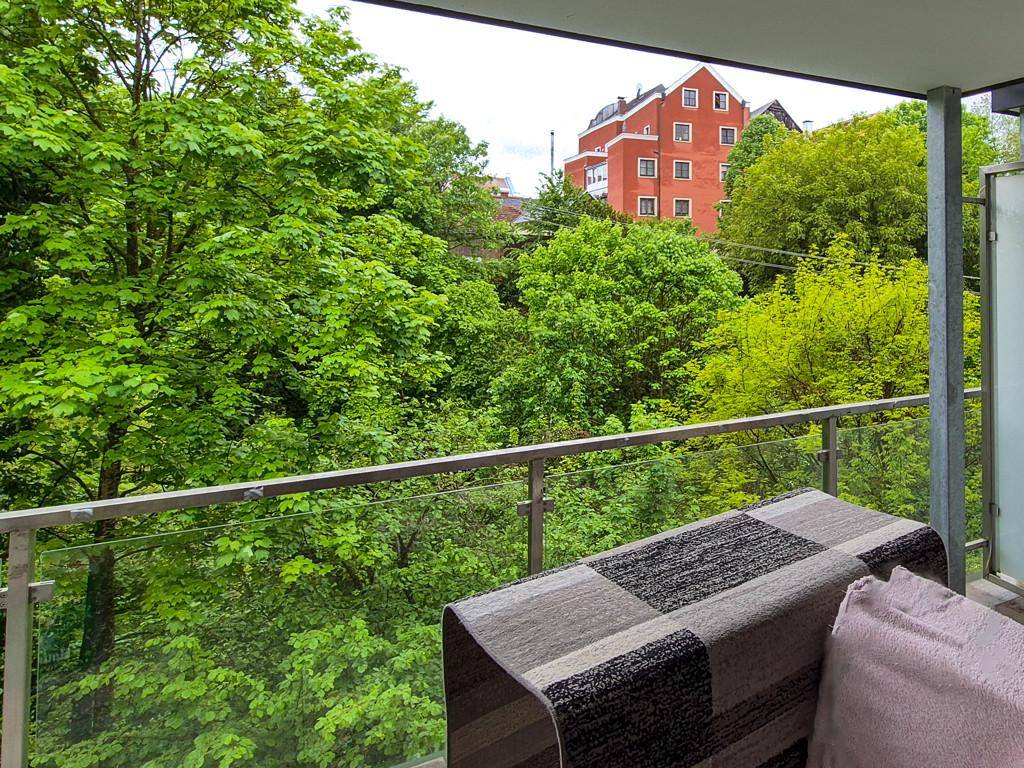 Balkon mit Glasgeländer bietet einen schönen Blick auf grüne Bäume und ein rotes Gebäude.