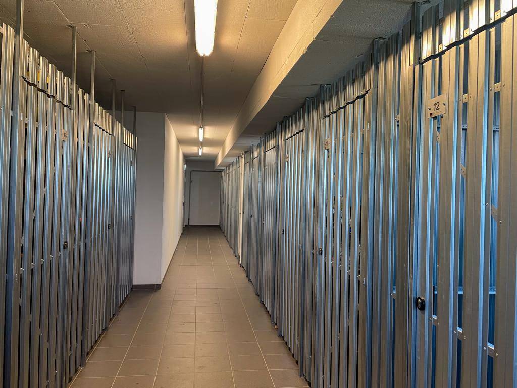 Langer Lagerraum mit Metallabtrennungen und Fliesenboden, ideal für zusätzlichen Stauraum.