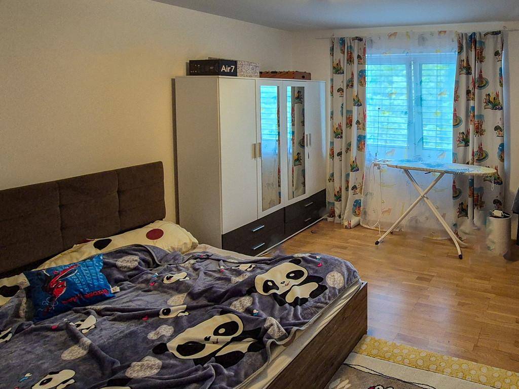 Schlafzimmer mit Bett, Kleiderschrank und Fenster, ausgestattet mit einem Holzboden.