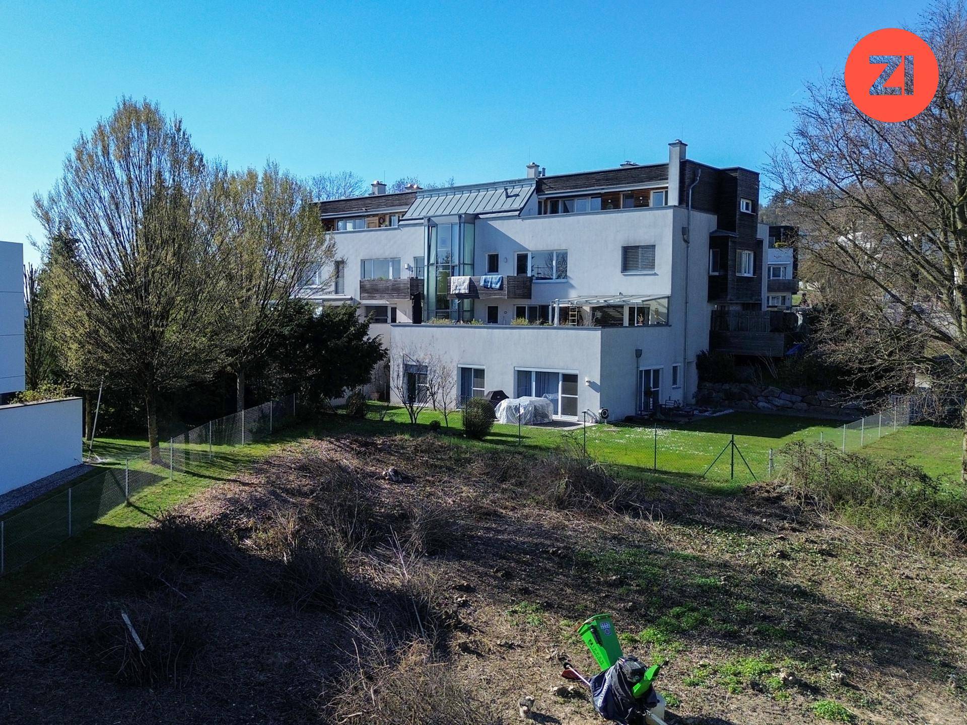 Mehrstöckiges Wohngebäude mit Balkonen und Terrassen, eingebettet in eine grüne Hanglage.