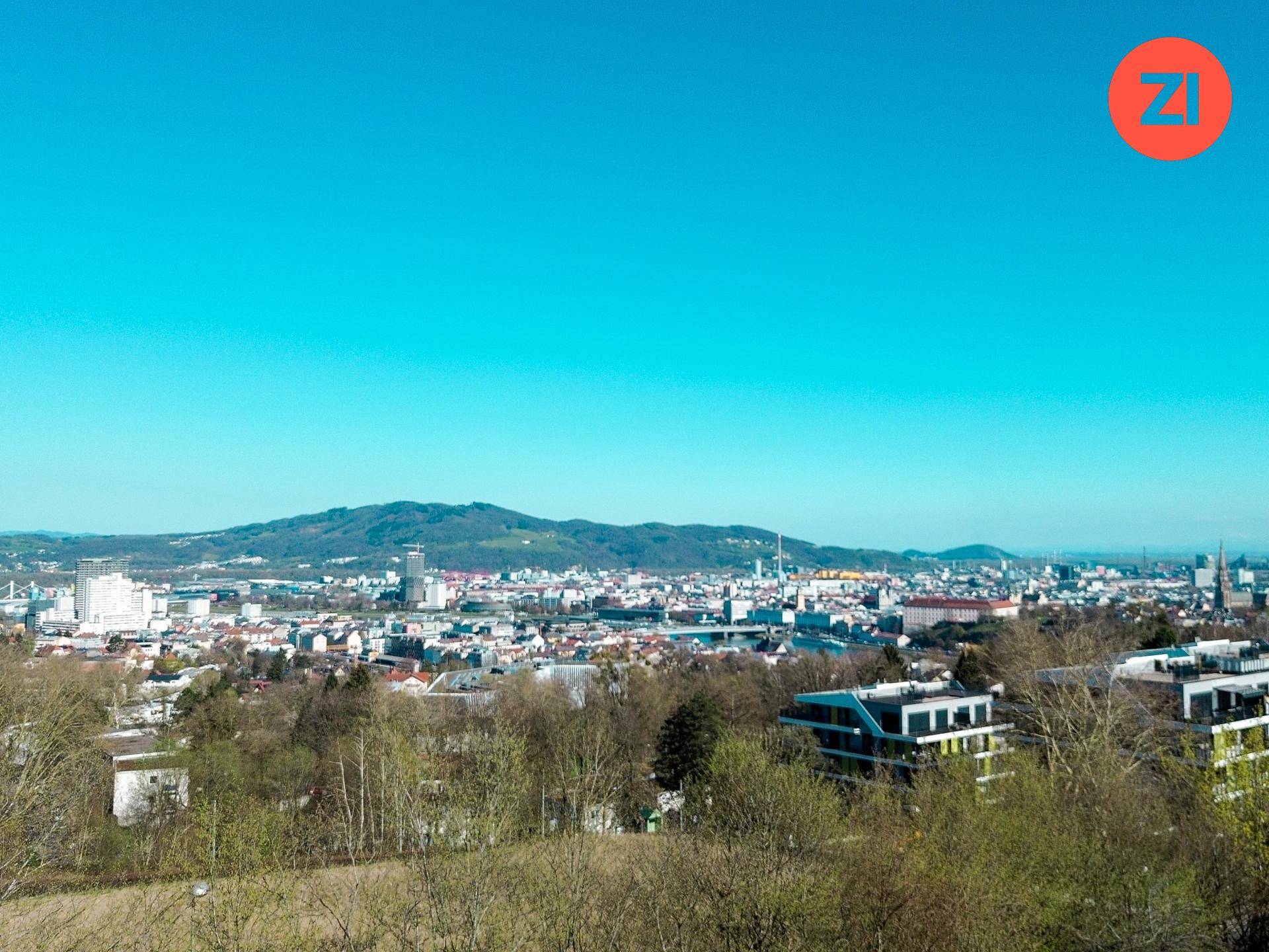 Panoramablick über eine Stadt mit Bergen im Hintergrund unter einem klaren blauen Himmel.