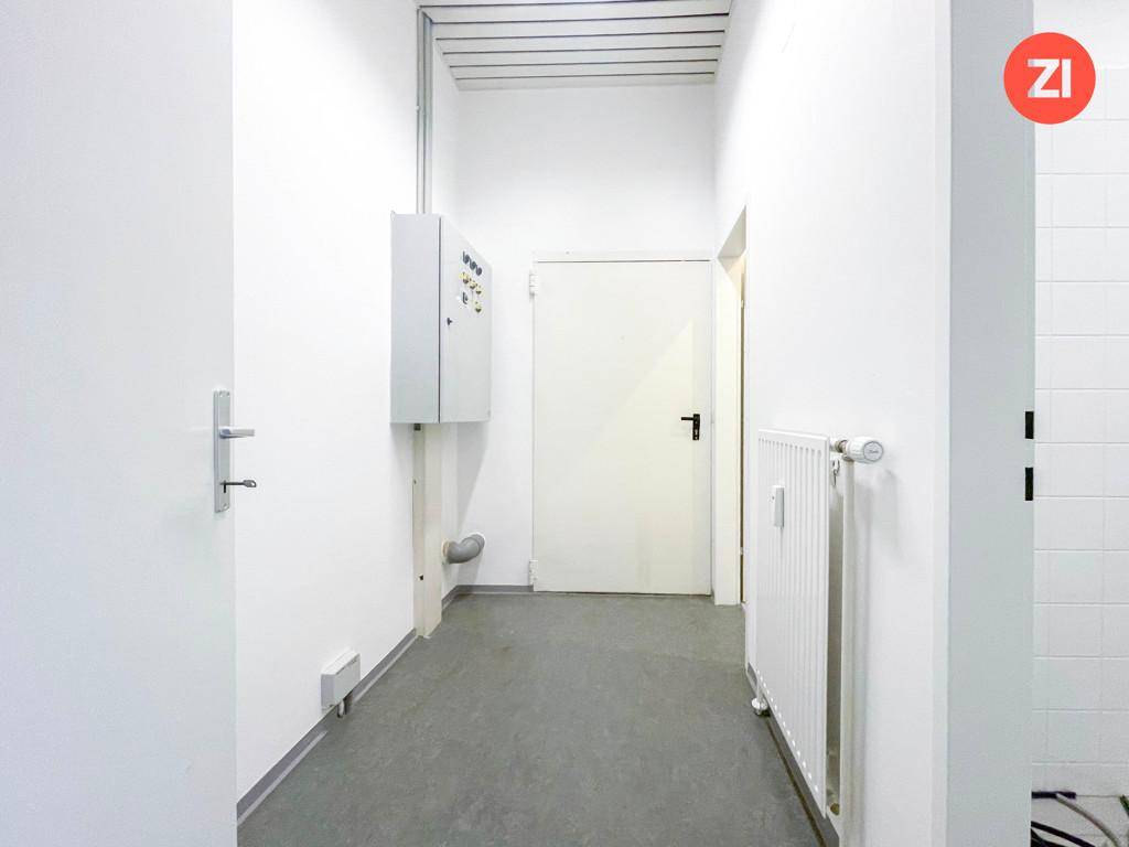 Schmaler Flur mit weiß gestrichenen Wänden, grauem Boden und einem Sicherungskasten.