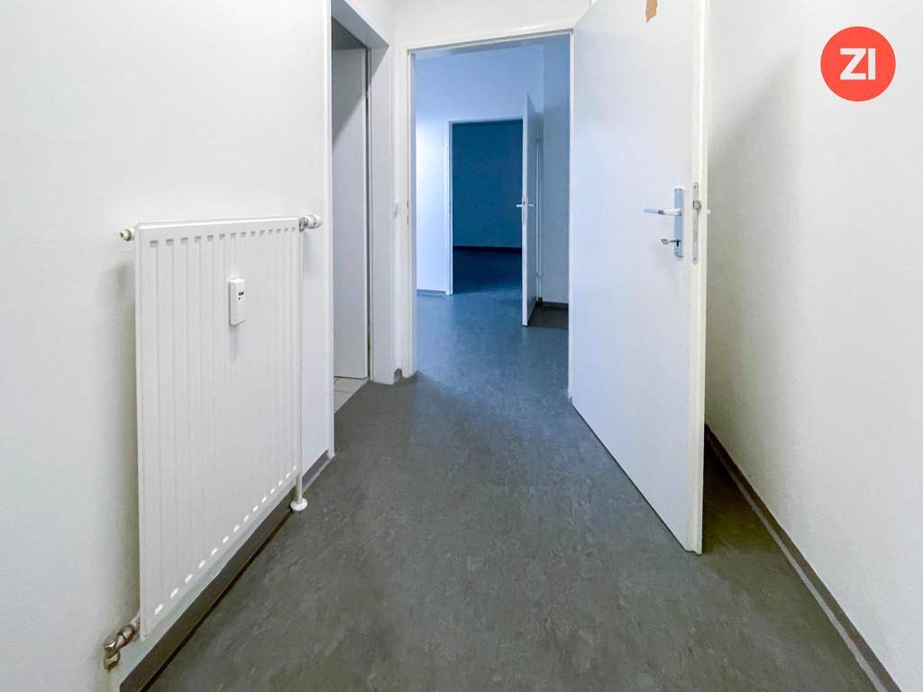 Heller Flur mit grauem Vinylboden, weiß gestrichenen Wänden und Heizkörper.