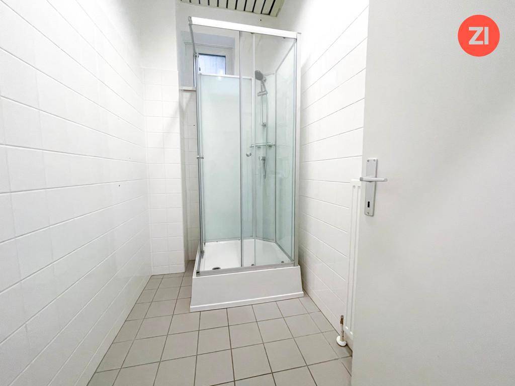 Badezimmer mit weiß gefliesten Wänden, grauem Fliesenboden und einer Duschkabine.