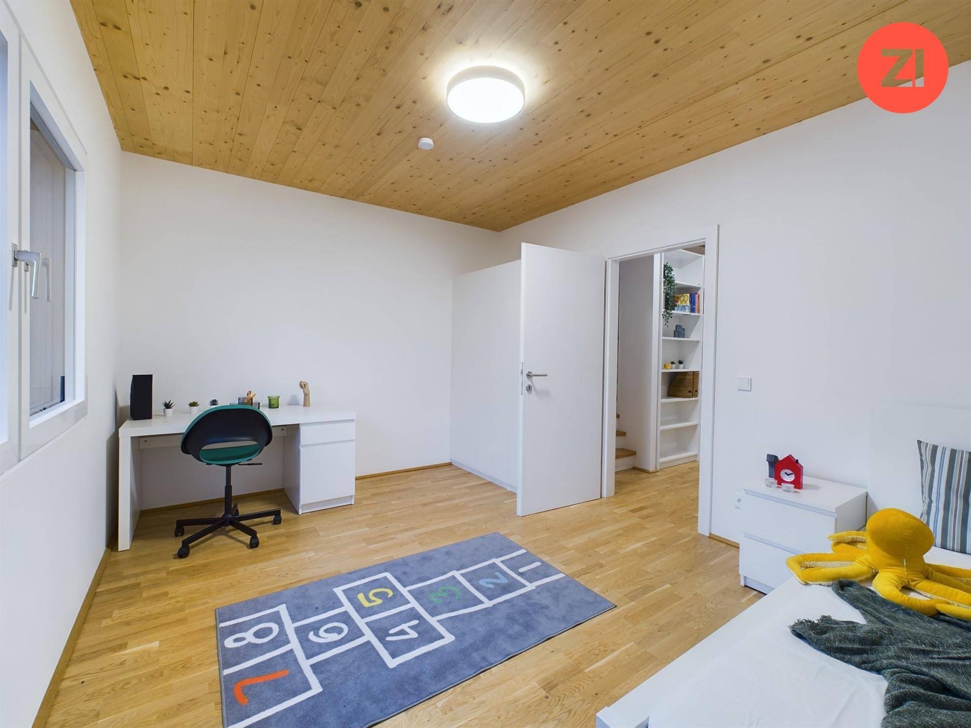 Freundliches Kinderzimmer mit Holzboden, Schreibtisch und einem bunten Spielteppich.