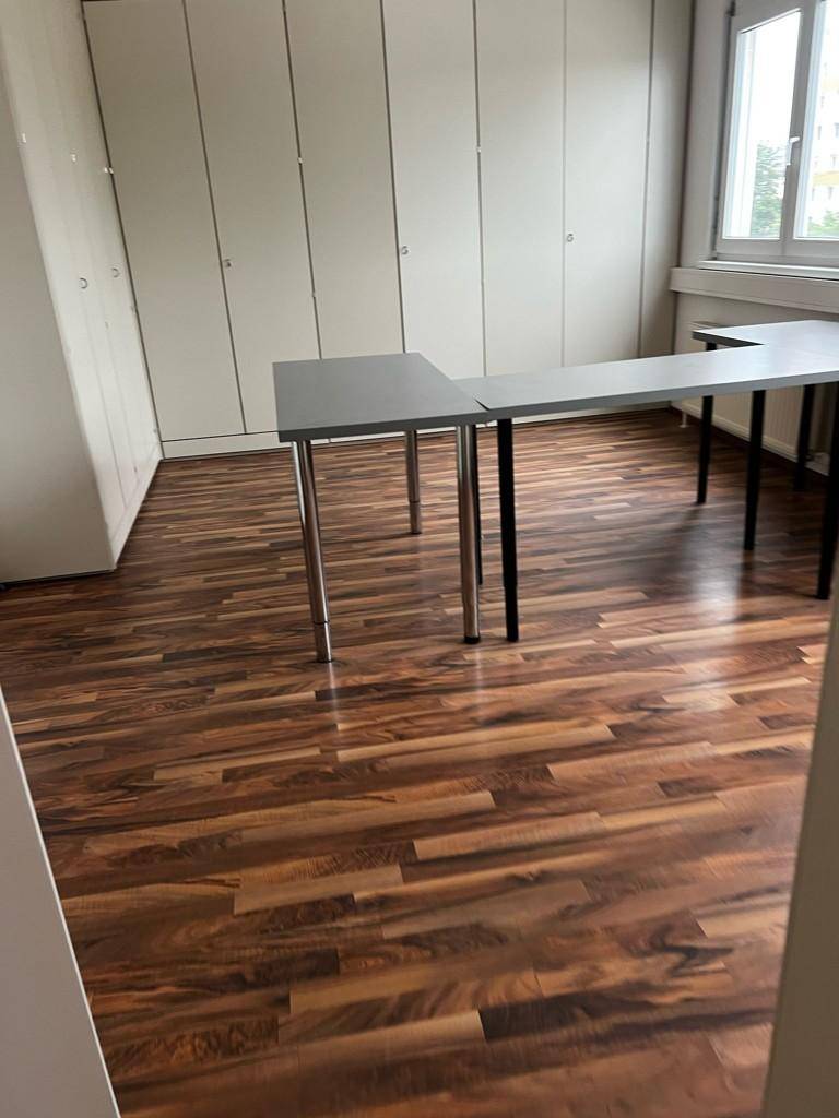 Büroraum mit Laminatboden, Einbauschränken und einem L-förmigen Schreibtisch, der den Arbeitsbereich definiert.