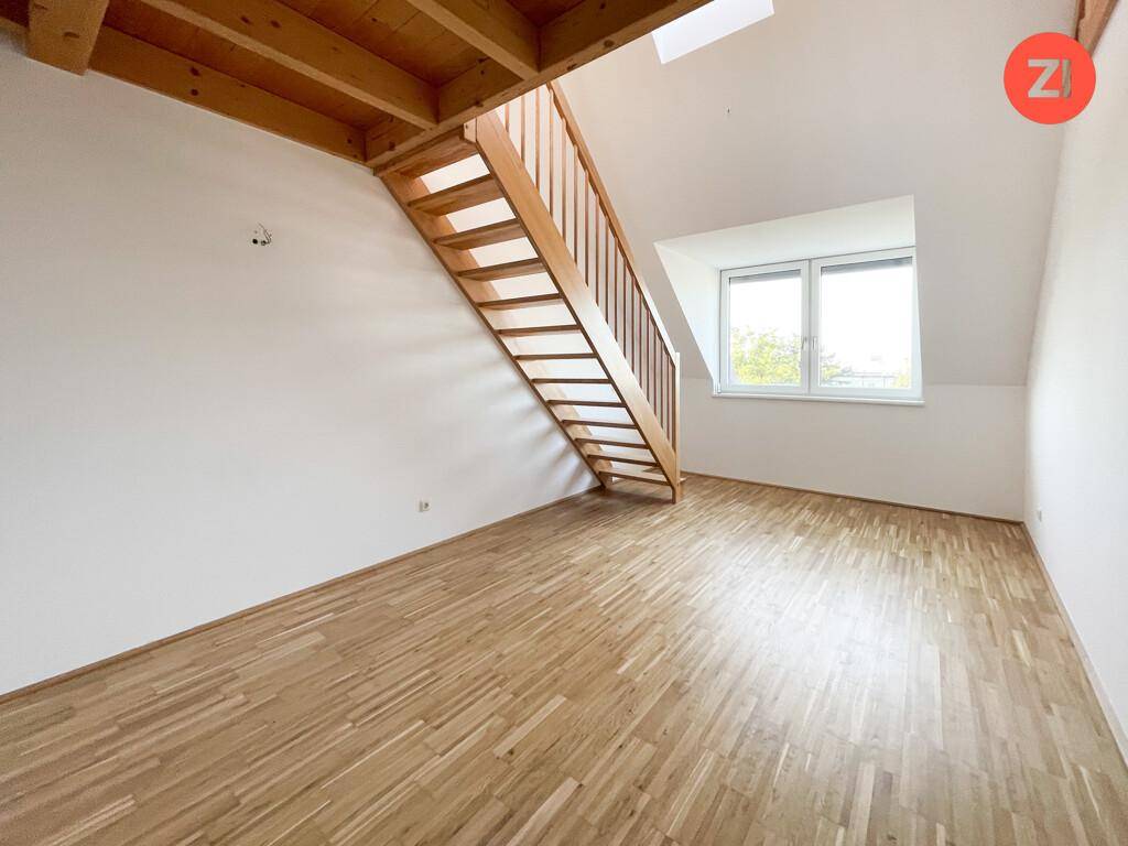 Heller Raum mit Holztreppe, Parkettboden und Fenster, unter sichtbaren Holzbalken im Dachgeschoss.